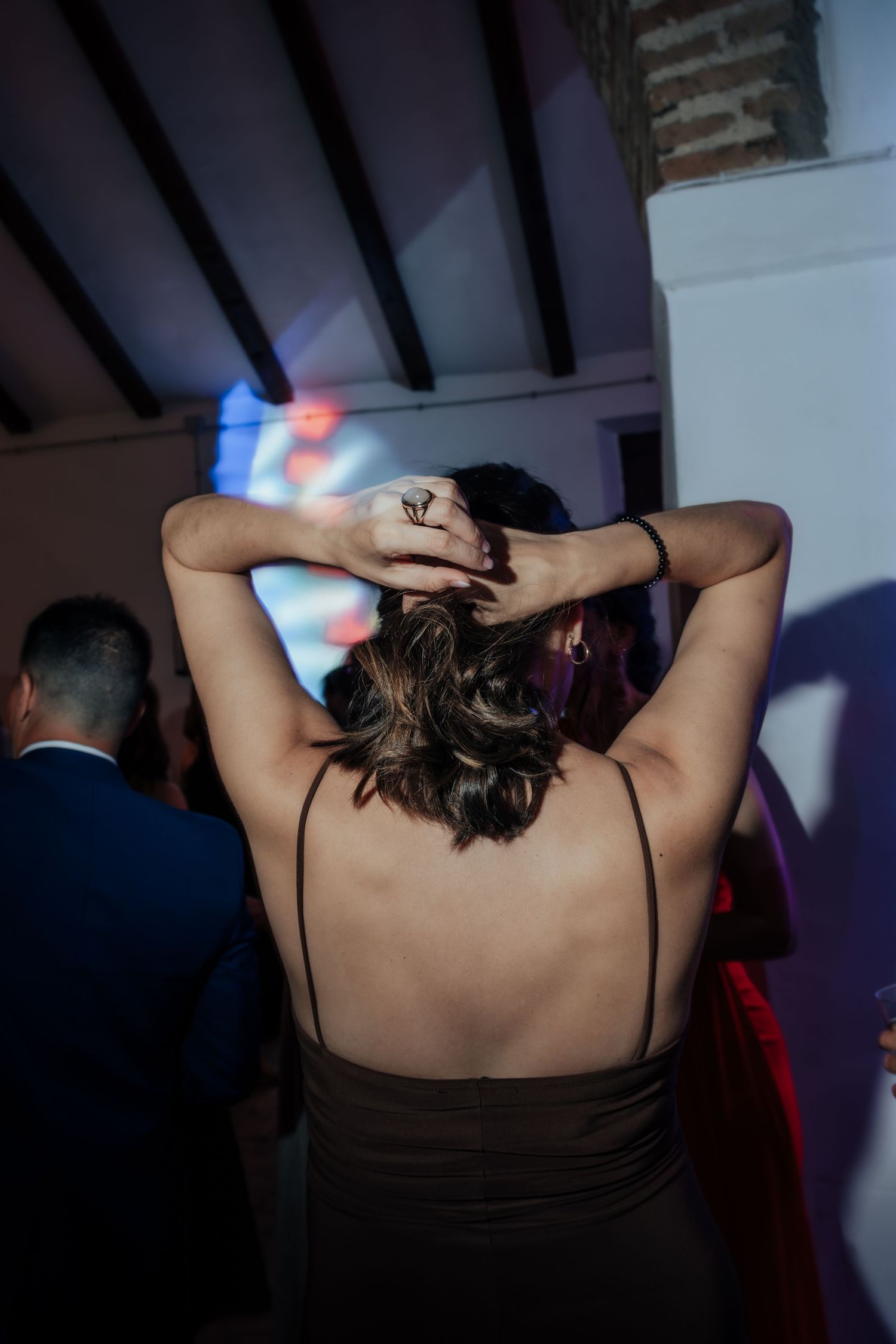 Woman in backless dress with hands in hair dancing at colorful wedding reception party.