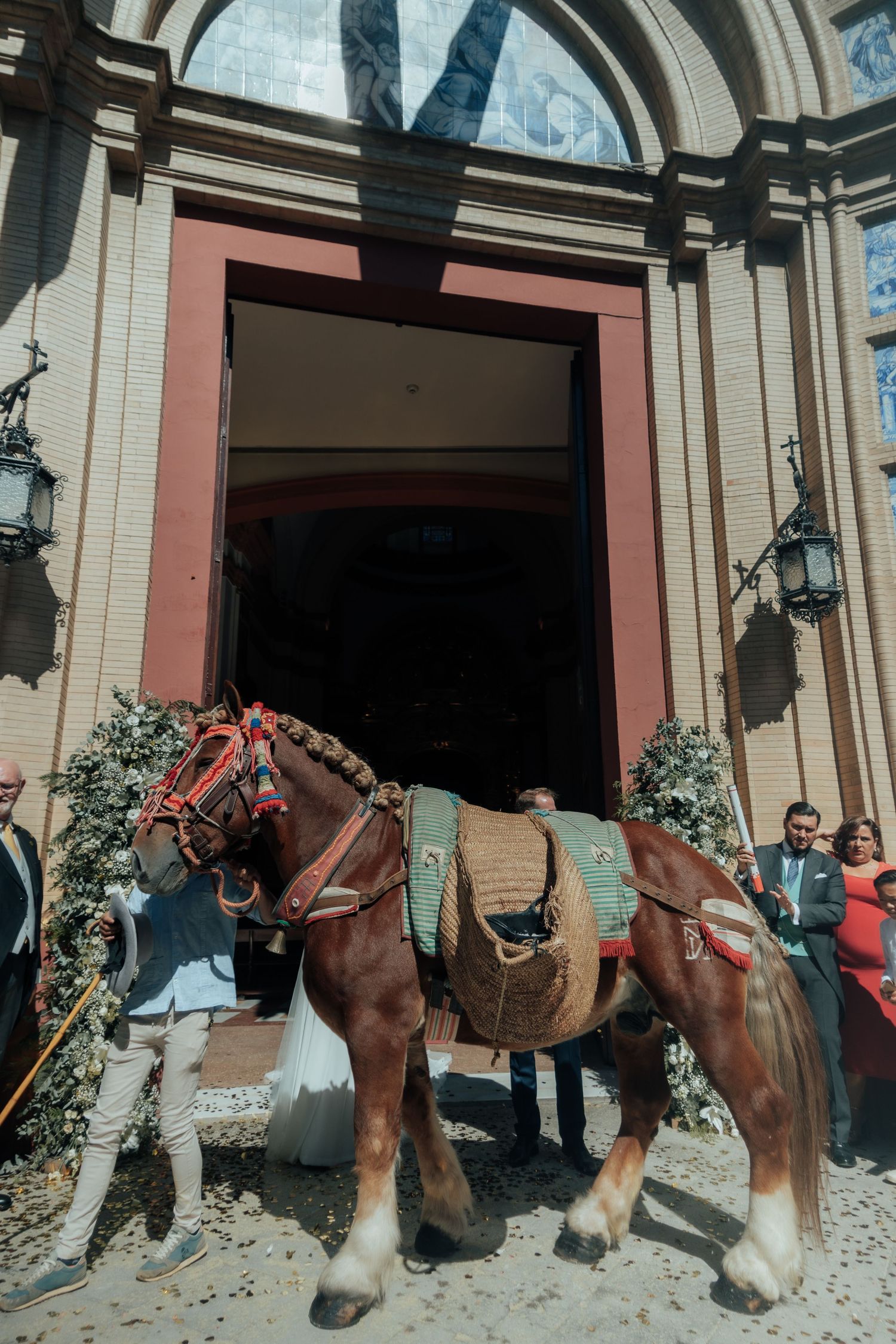 Decorated brown horse stands at entrance of church with blue tile panels at wedding.