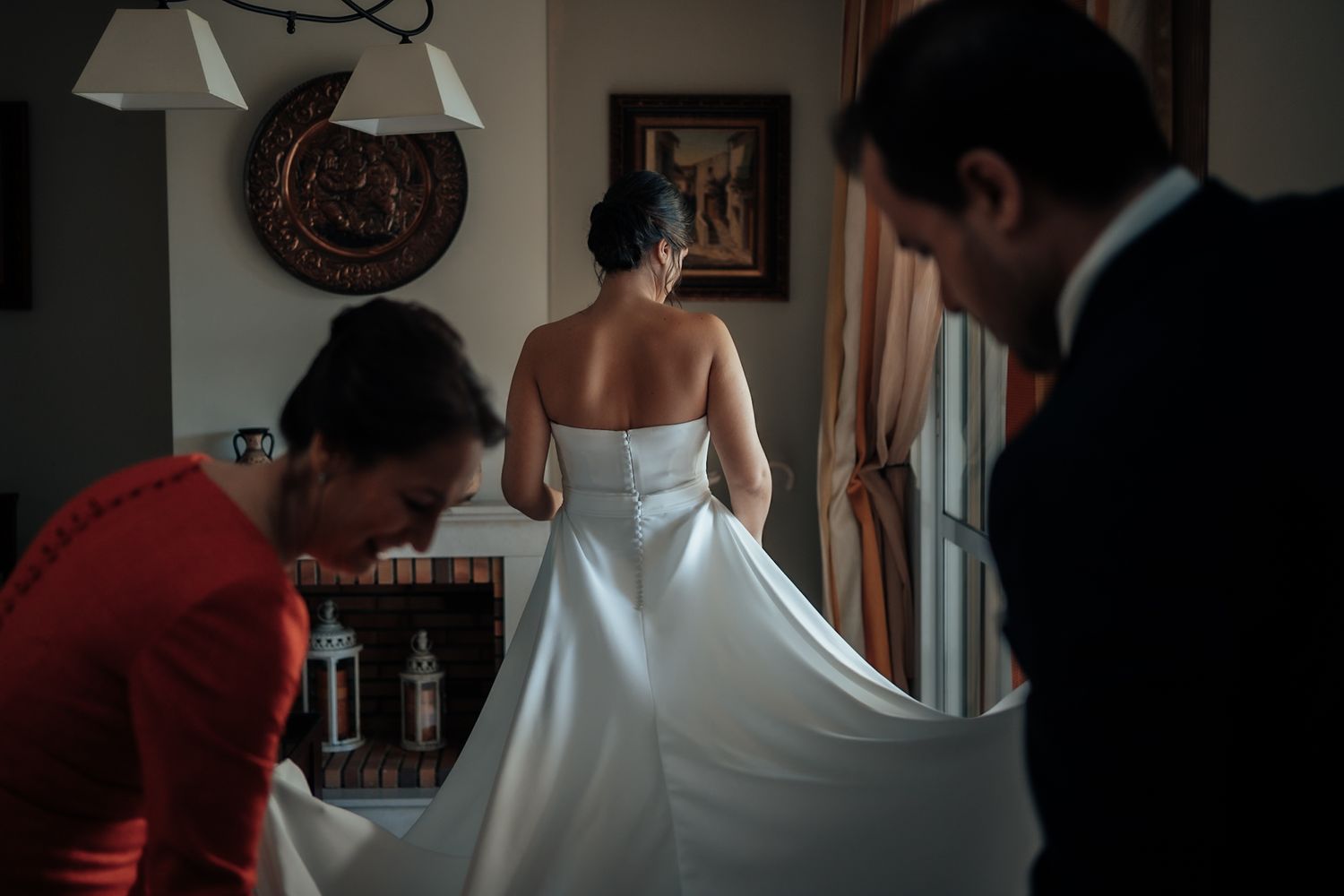 Bride in a strapless white gown being assisted by two helpers adjusting her dress before the ceremony.