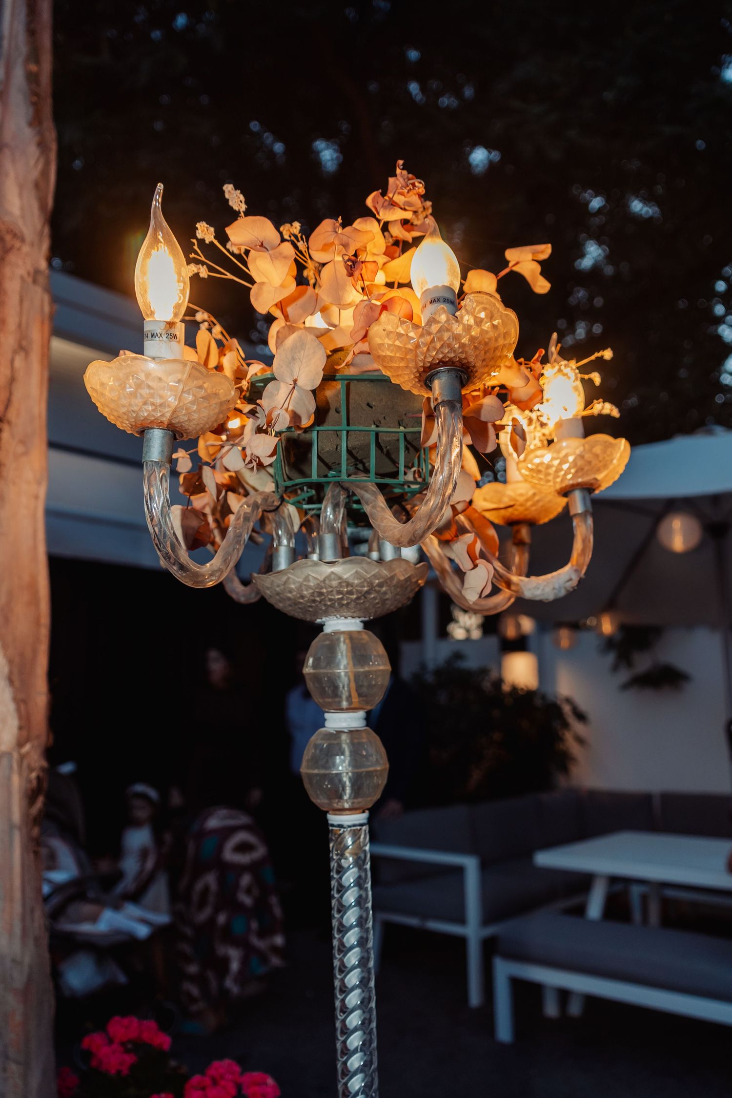 Ornate vintage candelabra lamp with floral decorations glowing warmly at an outdoor evening event.