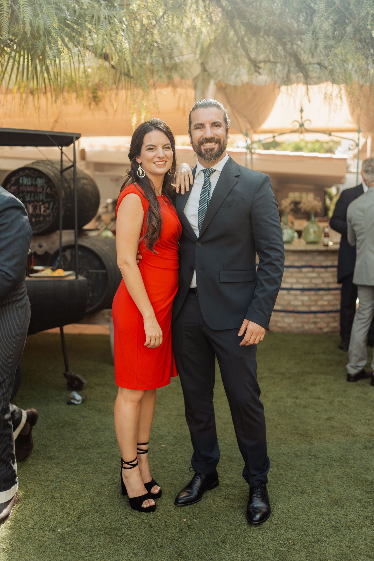 Couple posing at outdoor wedding, woman in red dress, man in dark suit.