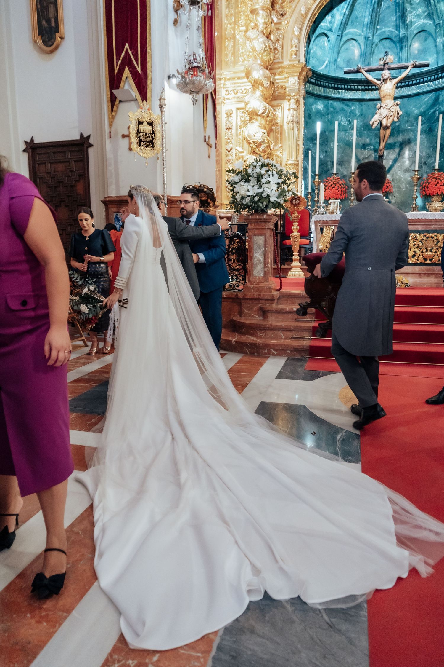 Bride with long cathedral train walking toward altar in ornate Spanish church wedding ceremony.