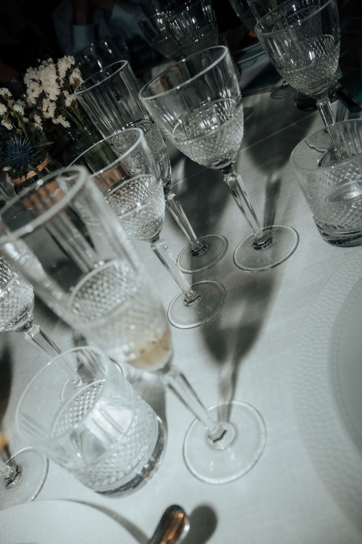 Elegant crystal champagne and wine glasses arranged on white linen tablecloth at formal wedding reception.