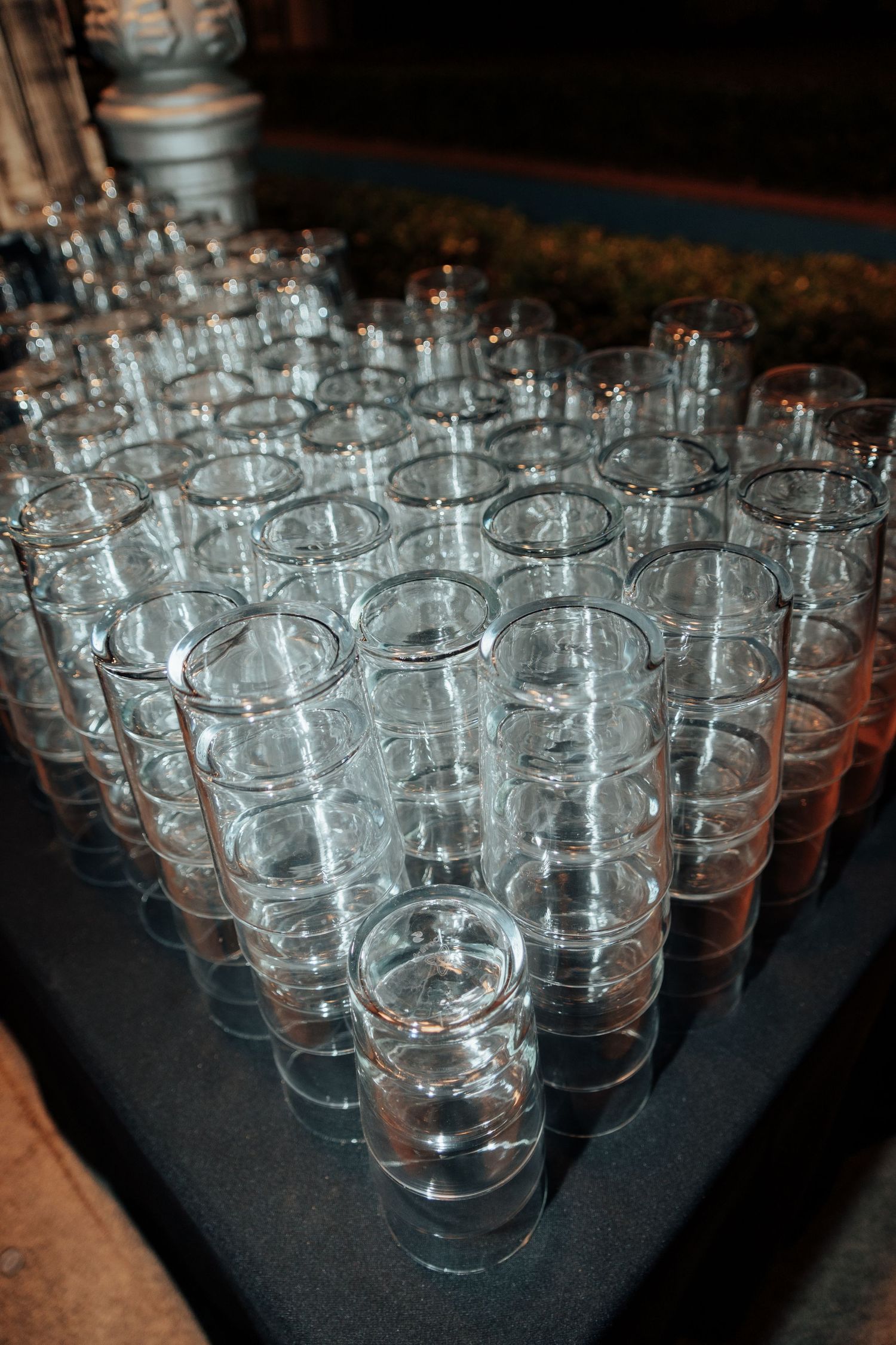 Rows of empty tall clear glass cups arranged in triangle formation on dark surface.