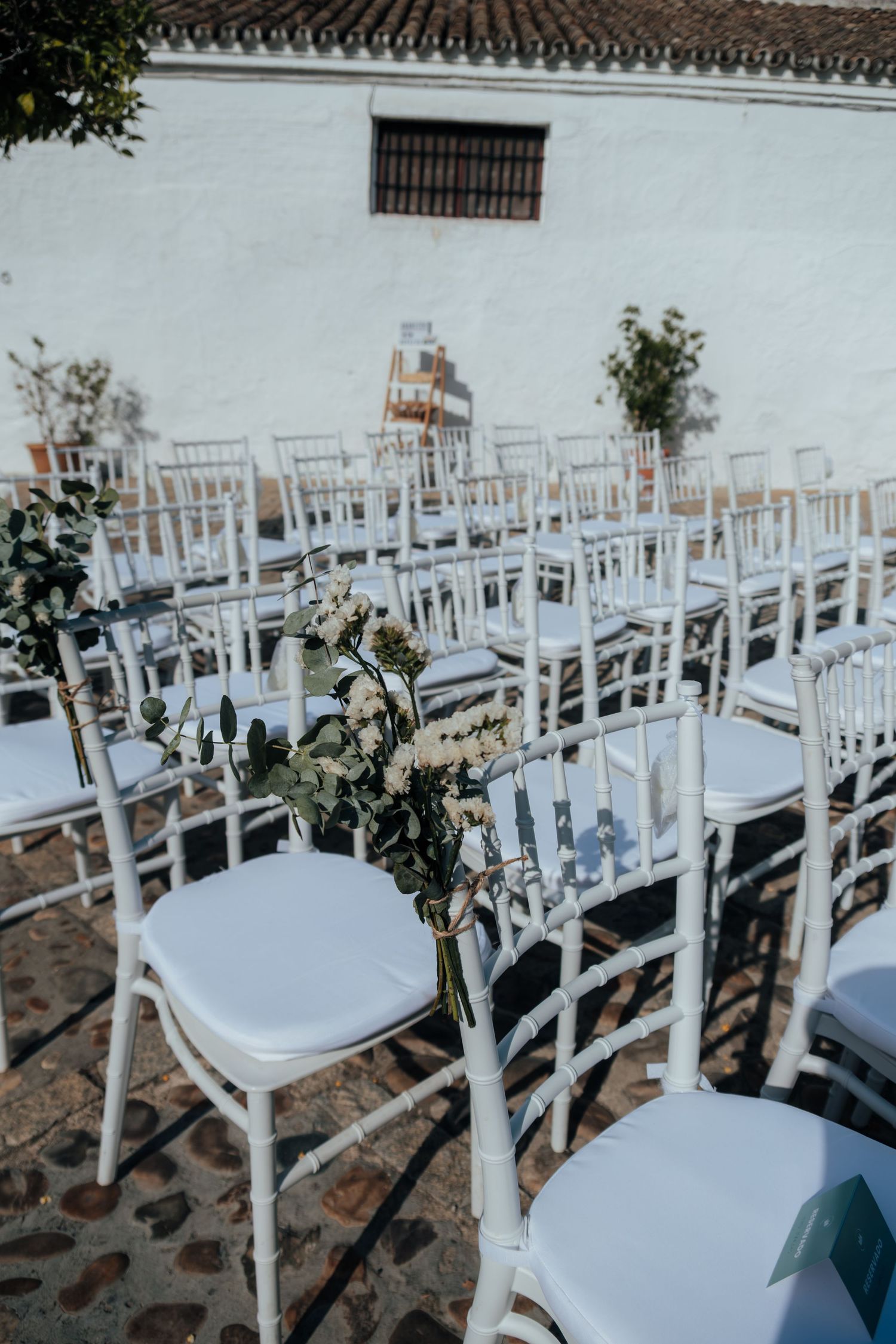 White Chiavari chairs arranged in rows for an outdoor wedding ceremony decorated with floral arrangements.