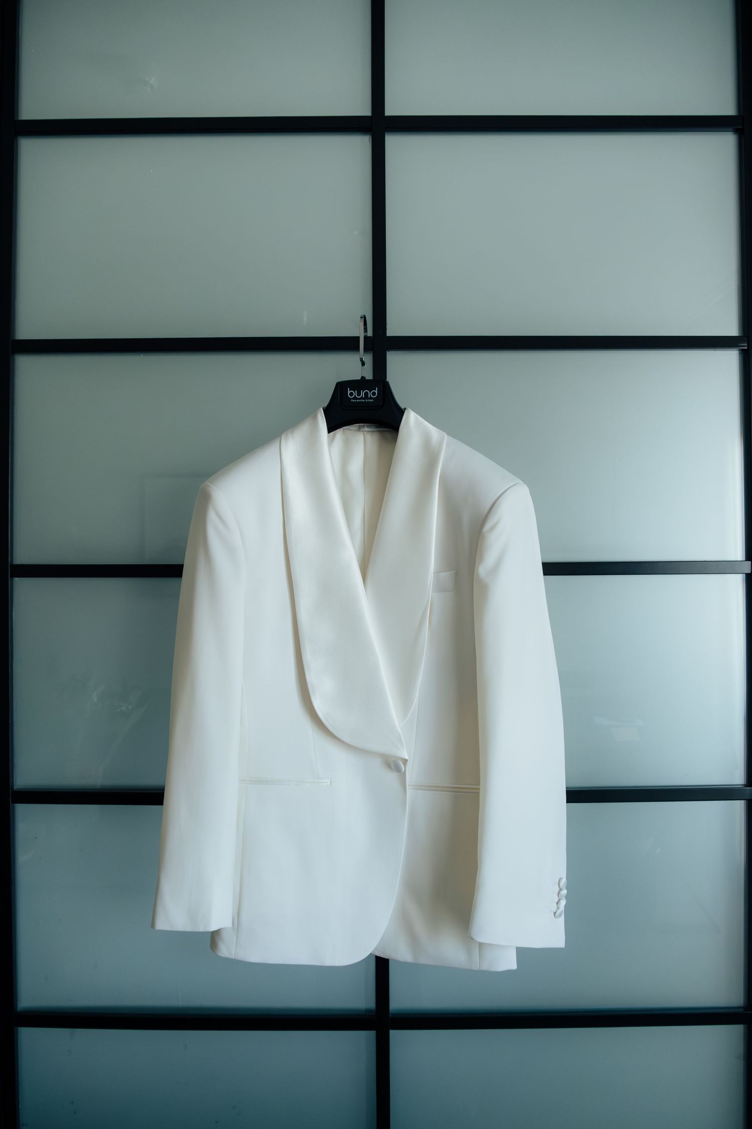 White formal blazer on a hanger displayed against a frosted glass panel background.