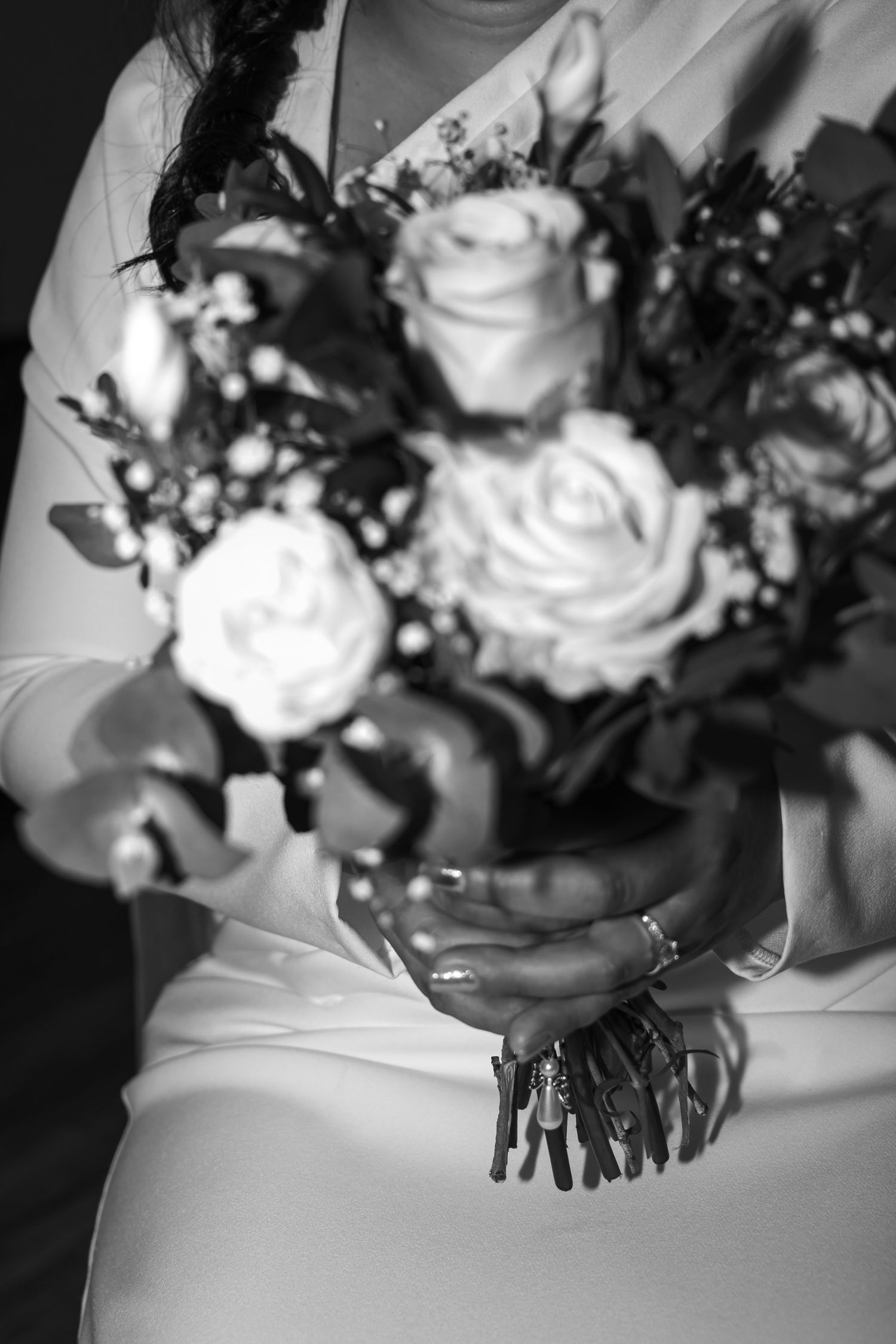 Black and white photo of bride holding rose bouquet with charm detail in both hands against white dress.