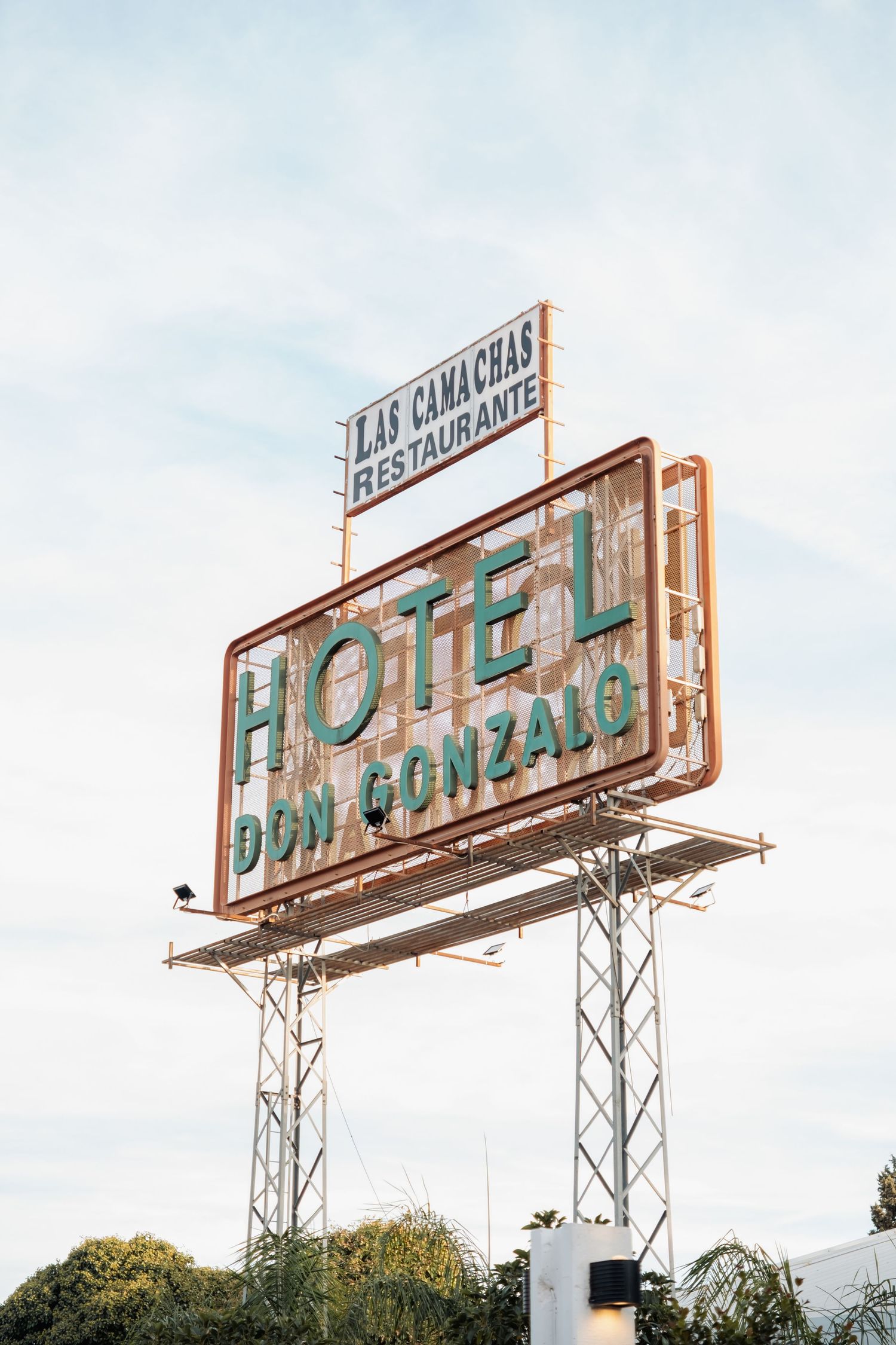 Vintage Hotel Don Gonzalo sign with Las Camachas Restaurante billboard against a cloudy sky.