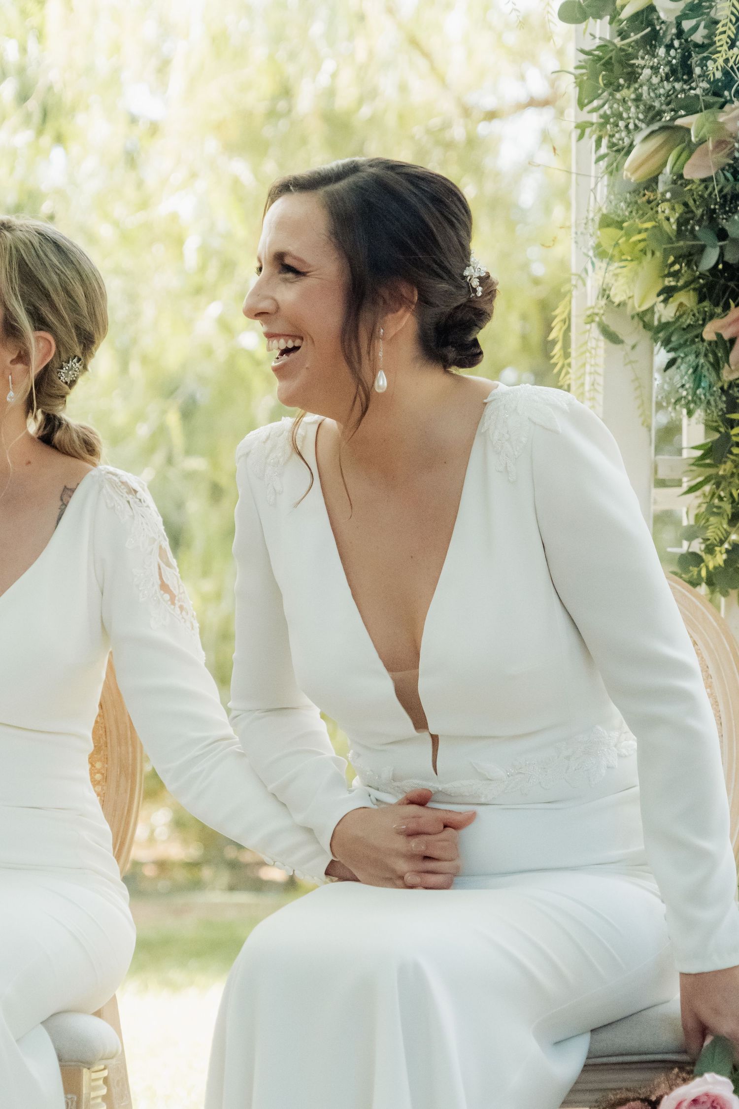 A joyful bride in an elegant white long-sleeve backless wedding dress laughs during her outdoor wedding ceremony.