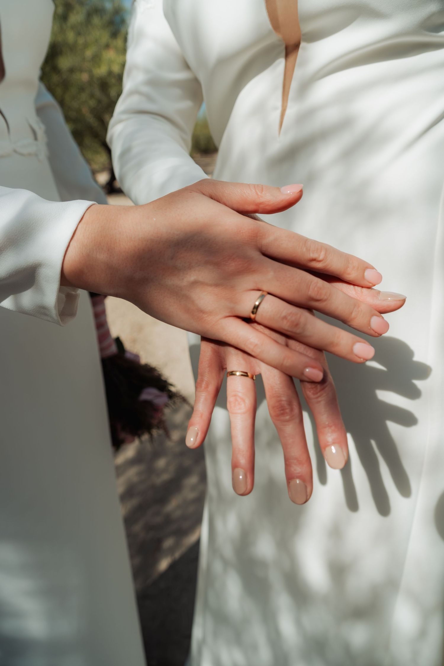 Close-up of two brides showing off their gold wedding rings on their hands in white gowns.