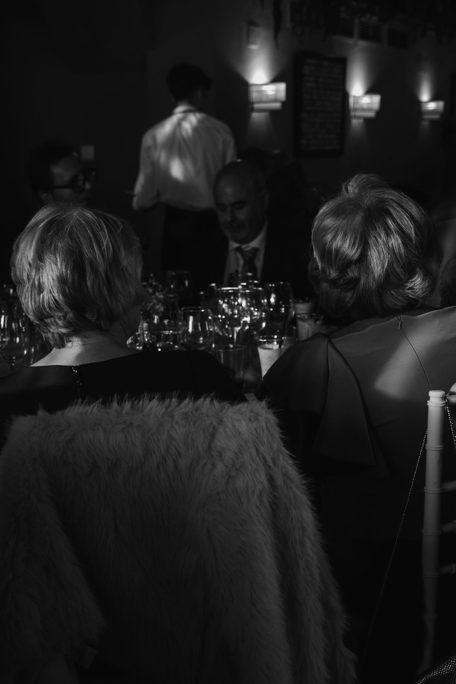 Wedding reception dinner guests seated at candlelit table in dark venue.