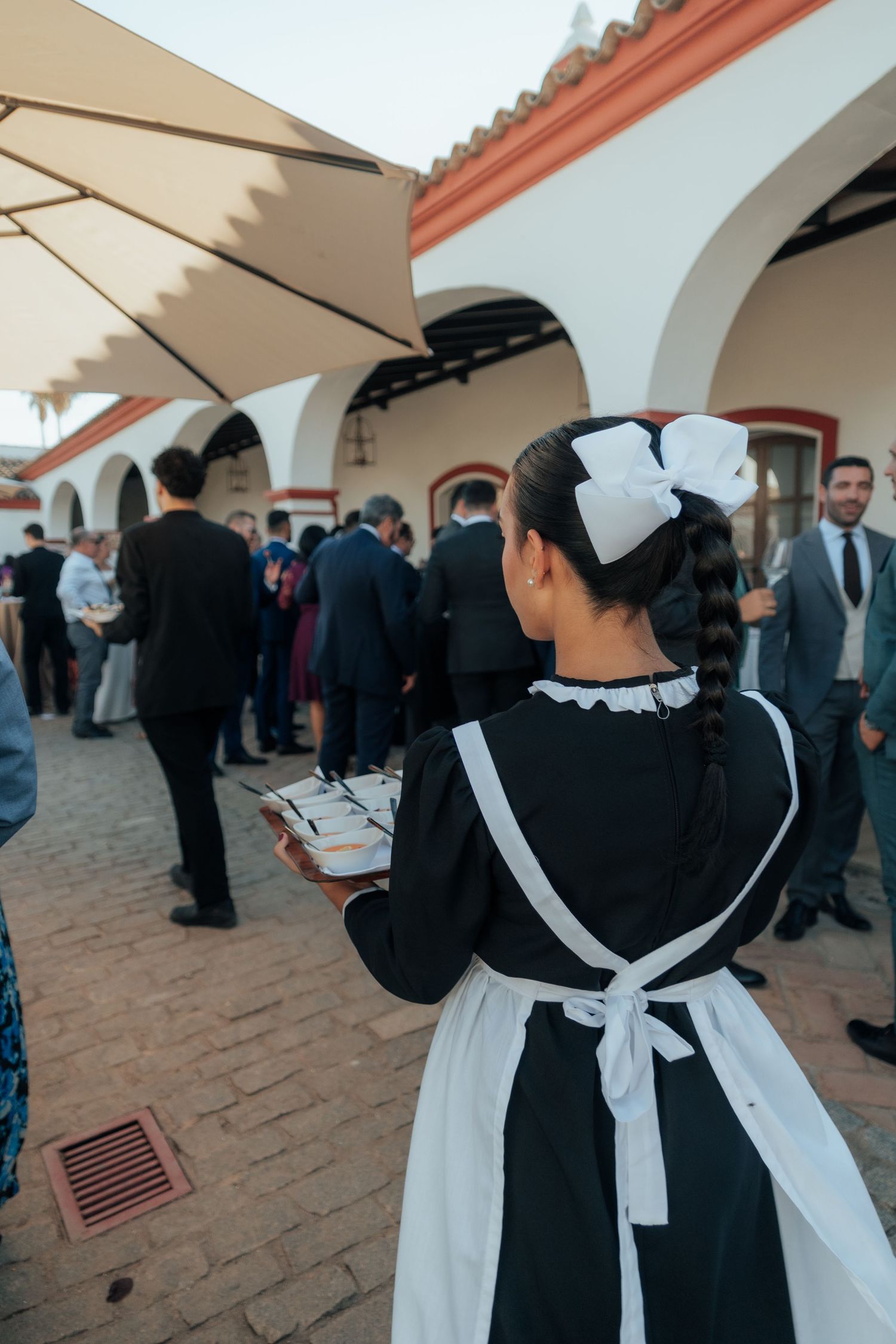 Waitress in black and white maid uniform carrying a tray at an outdoor wedding reception.
