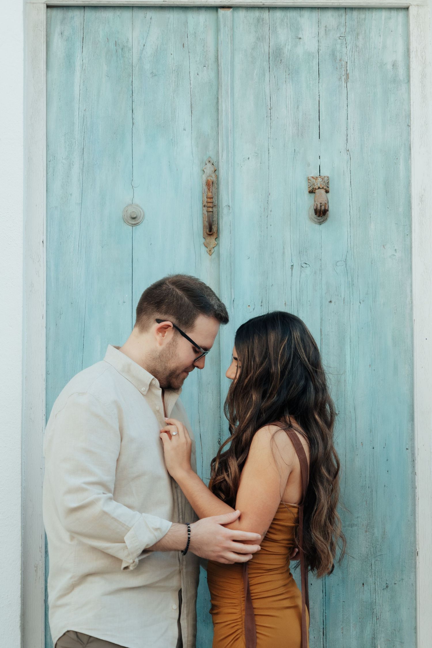 Couple sharing a tender moment in front of a rustic turquoise wooden door, woman in mustard dress.