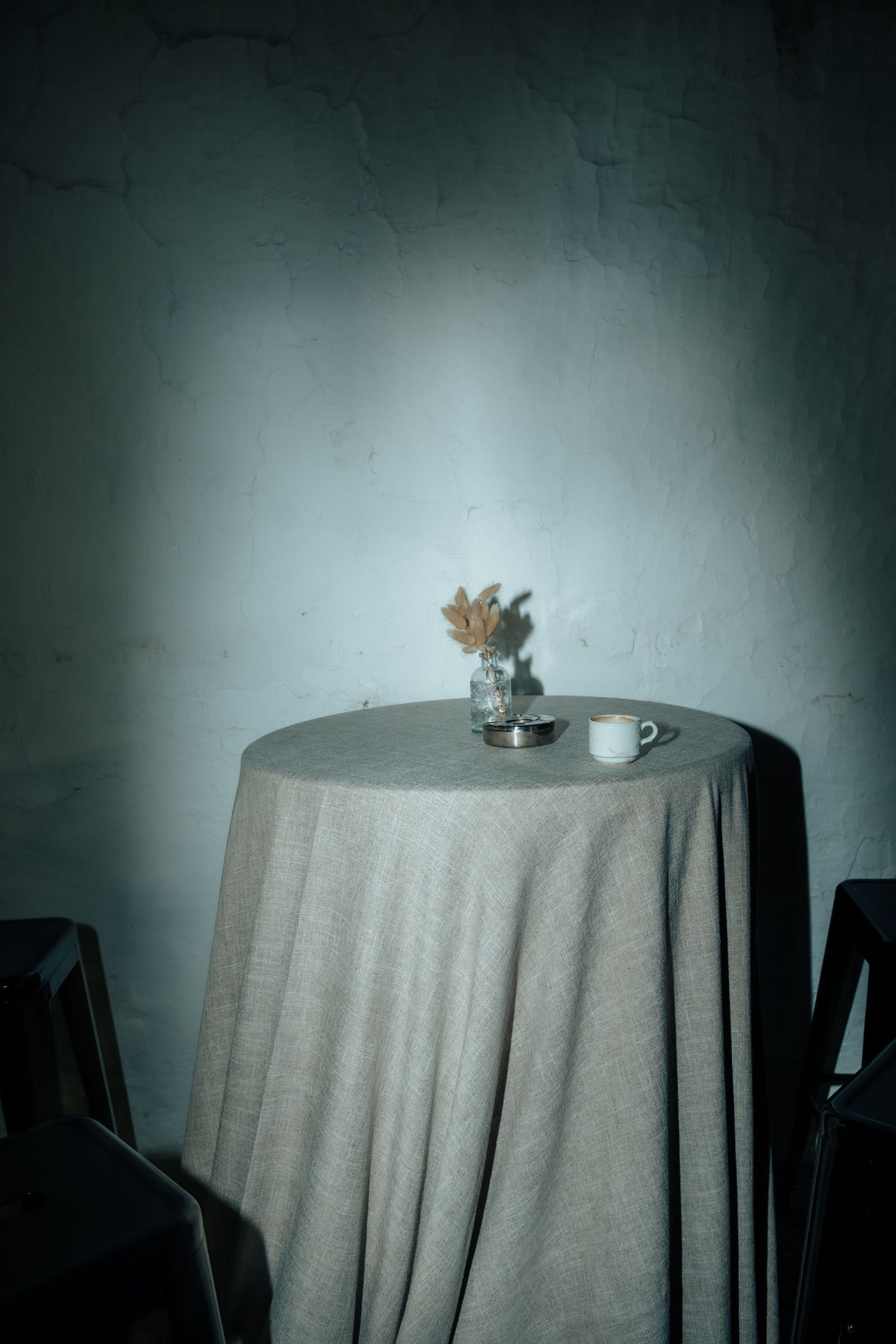 Round table with linen drape, dried flowers vase and white cup against white wall.