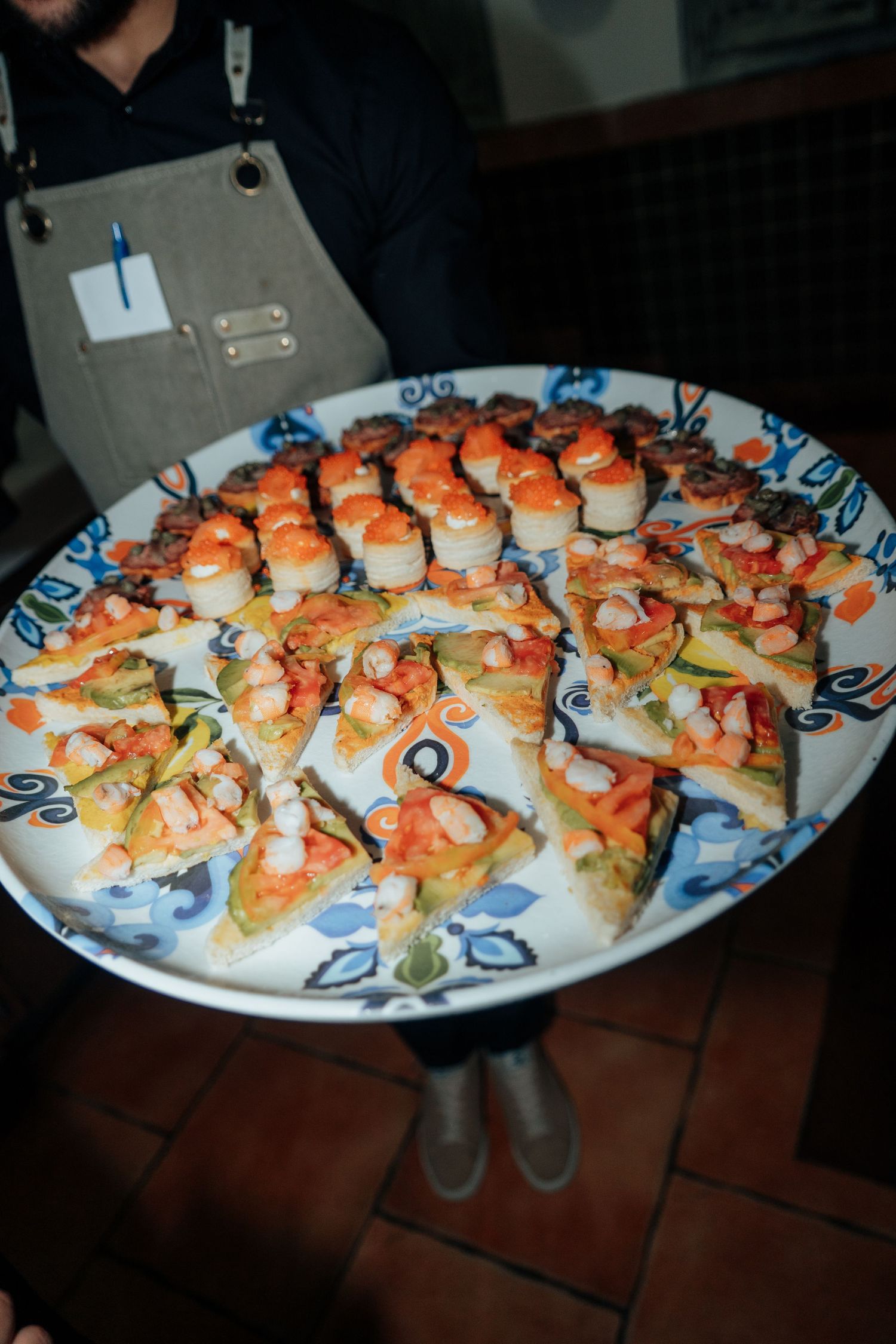 Waiter serving a large decorative platter of seafood appetizers and canapes at a catered event.