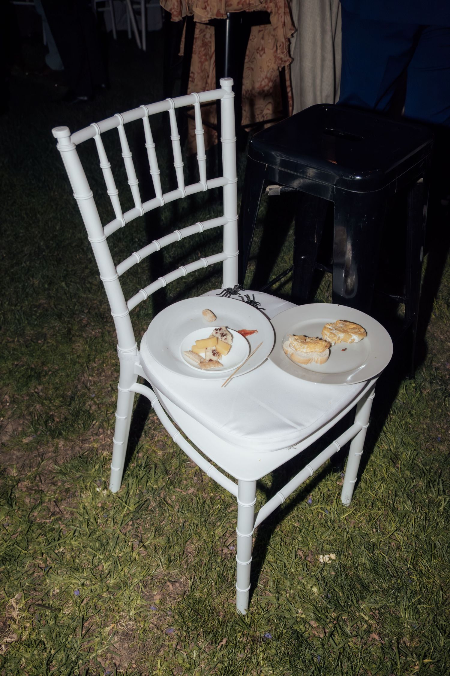 Two white plates with desserts resting on a white Chiavari chair on grass at an outdoor event.