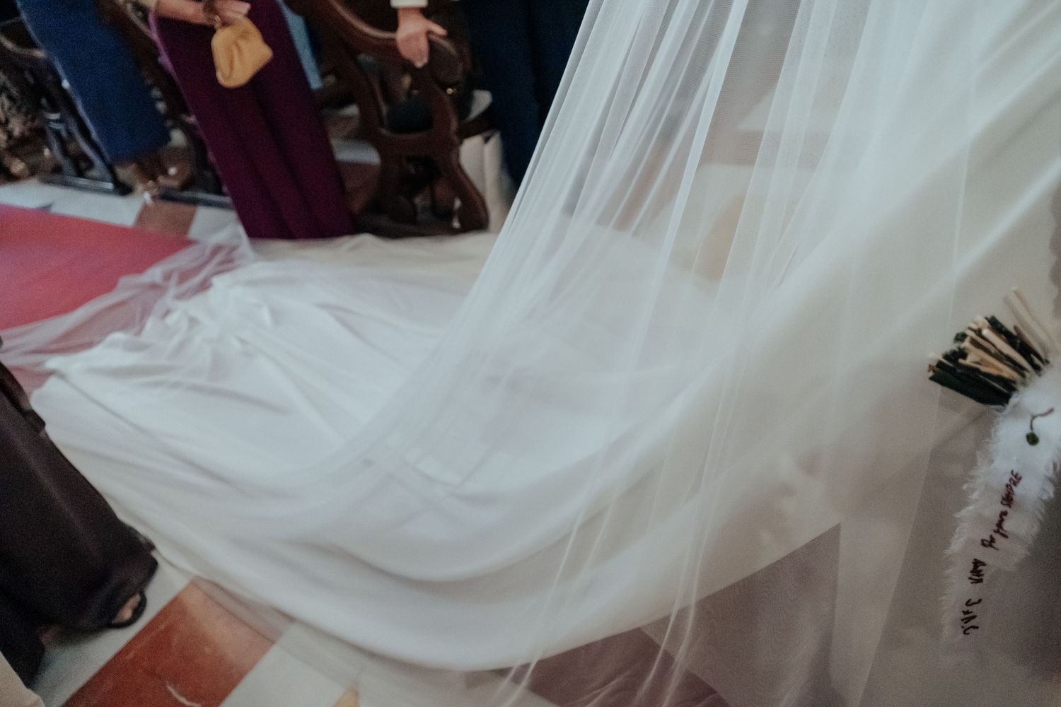 Close-up of flowing white bridal veil train spread across church aisle floor.