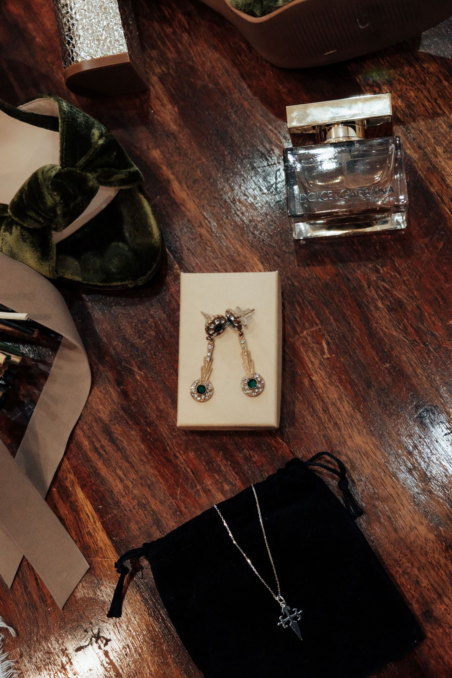 Wedding flat lay featuring gold earrings, silver necklace, Dolce and Gabbana perfume on wood table.