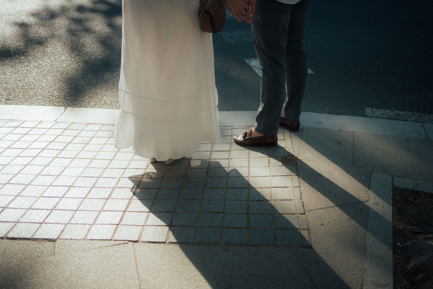 Shadows of a wedding couple cast on sunlit tiled pavement, bride in white gown and groom in grey suit.