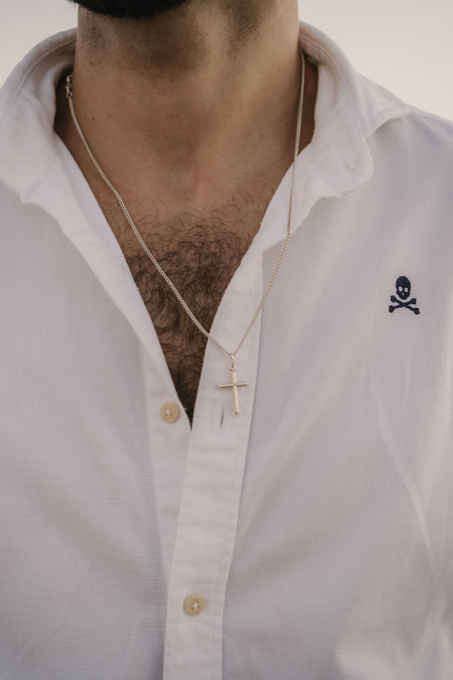 Close-up of man in white shirt with skull logo wearing a gold cross pendant necklace on a chain.