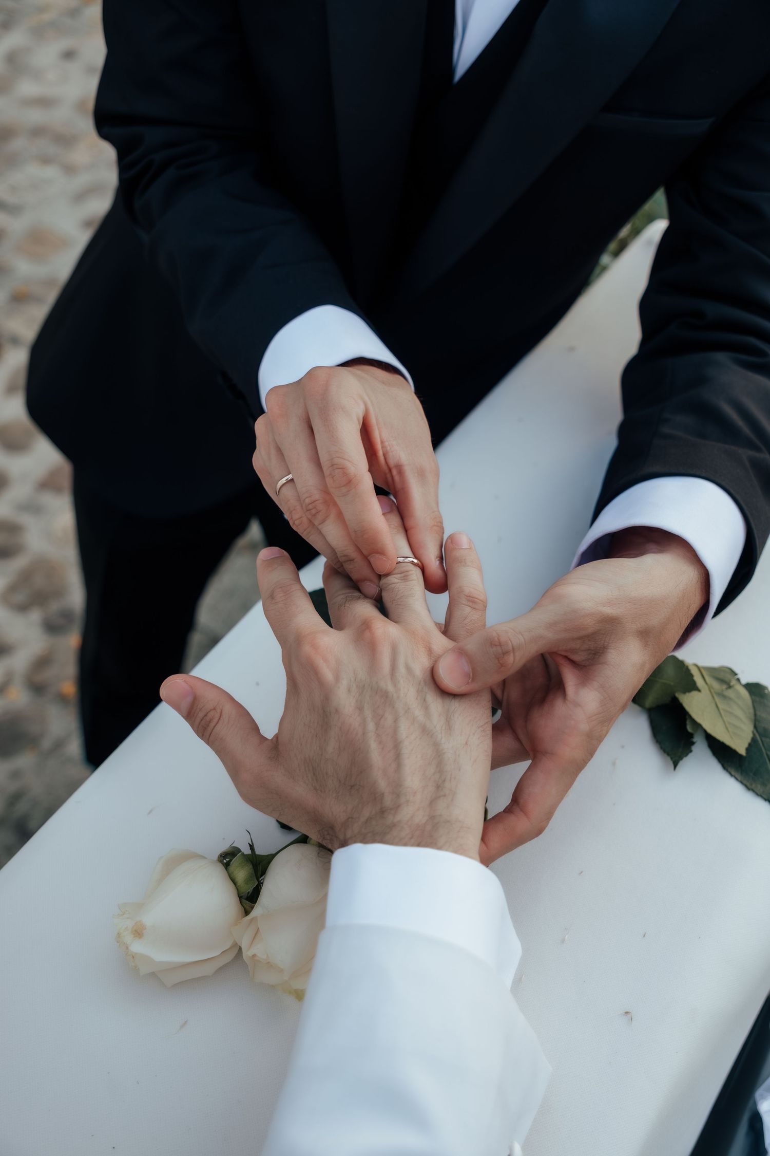 Grooms exchanging wedding rings at altar with white rose during same-sex wedding ceremony.
