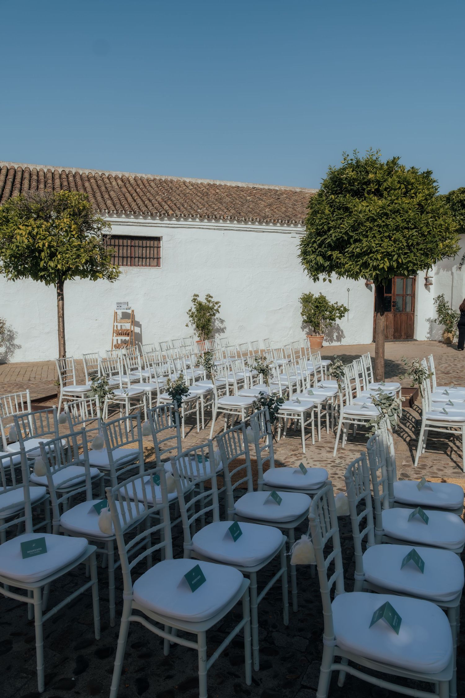 Rows of white Chiavari chairs set up in a sunlit courtyard for an elegant outdoor wedding ceremony.