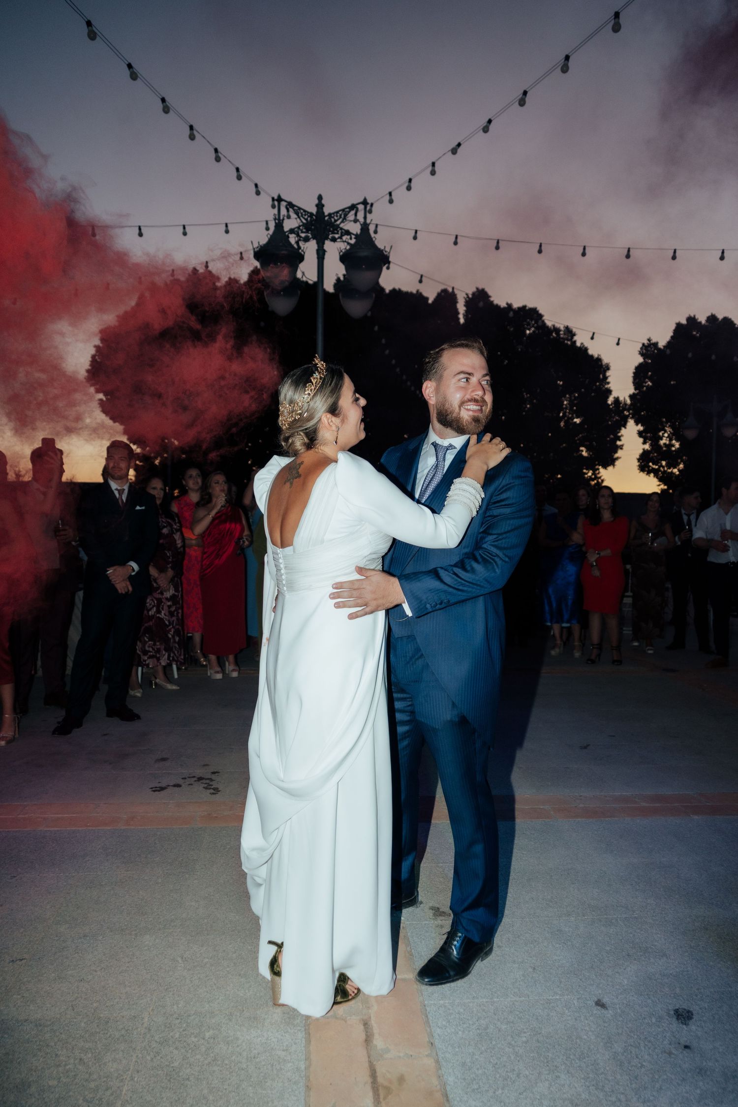 Bride and groom sharing first dance outdoors at sunset with colorful smoke bomb backdrop.