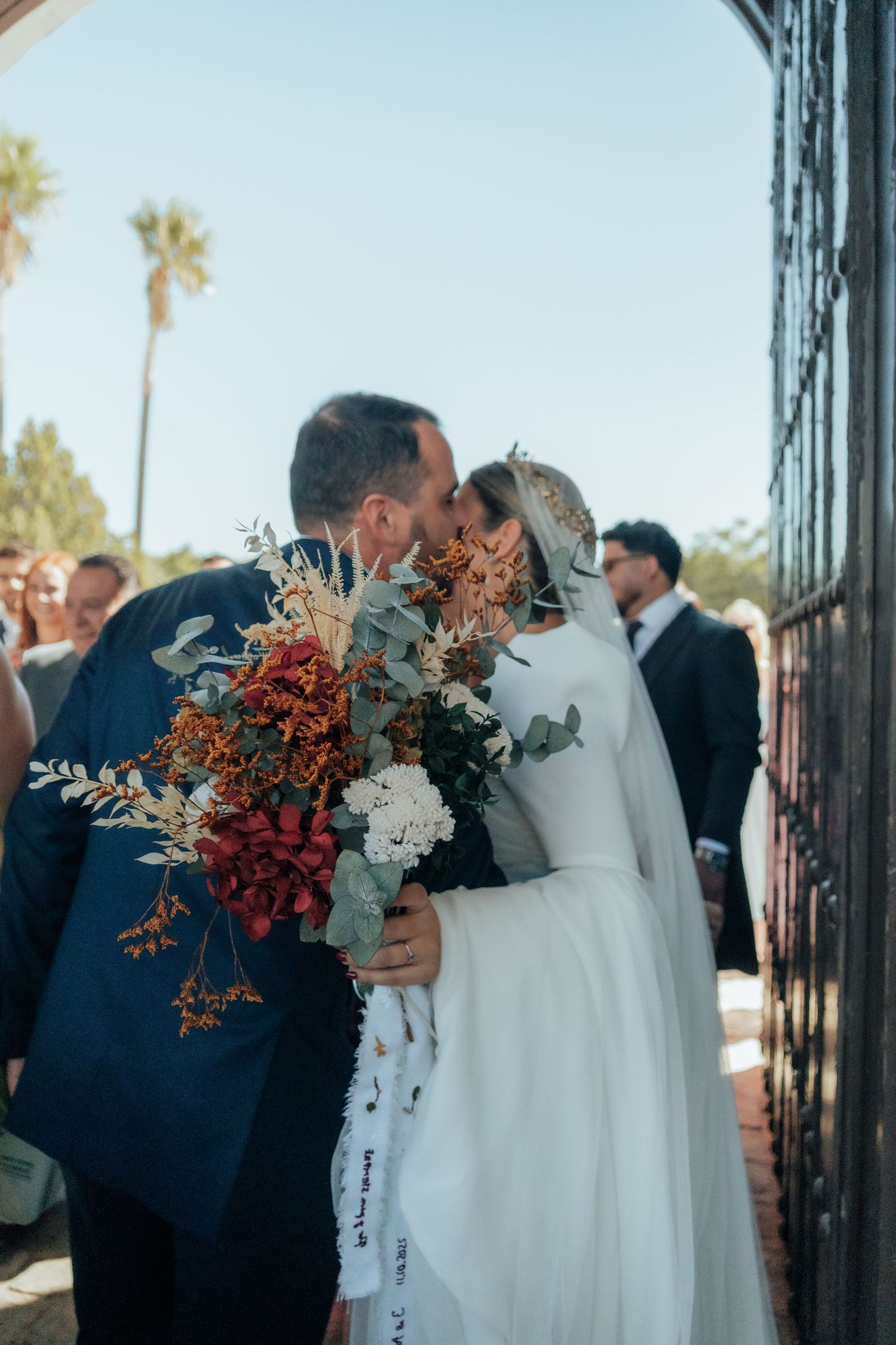 Bride and groom share a romantic kiss at hacienda gates holding a beautiful autumn bridal bouquet.
