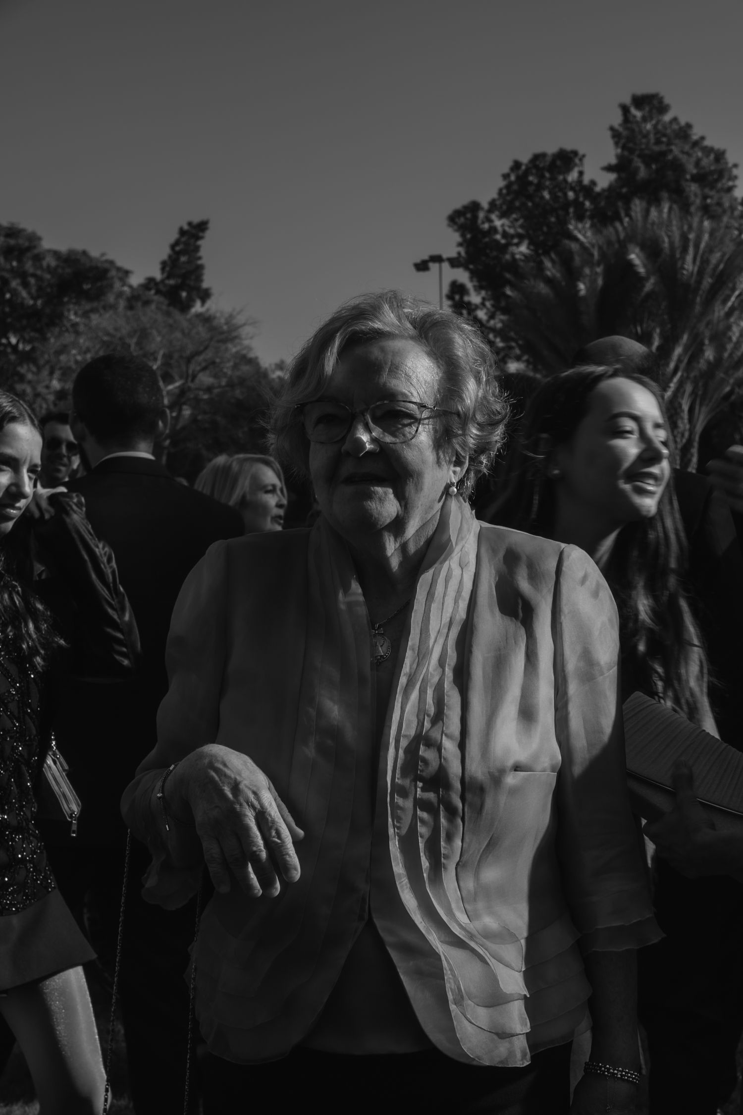 Black and white photo of elderly woman smiling at outdoor wedding event surrounded by guests.