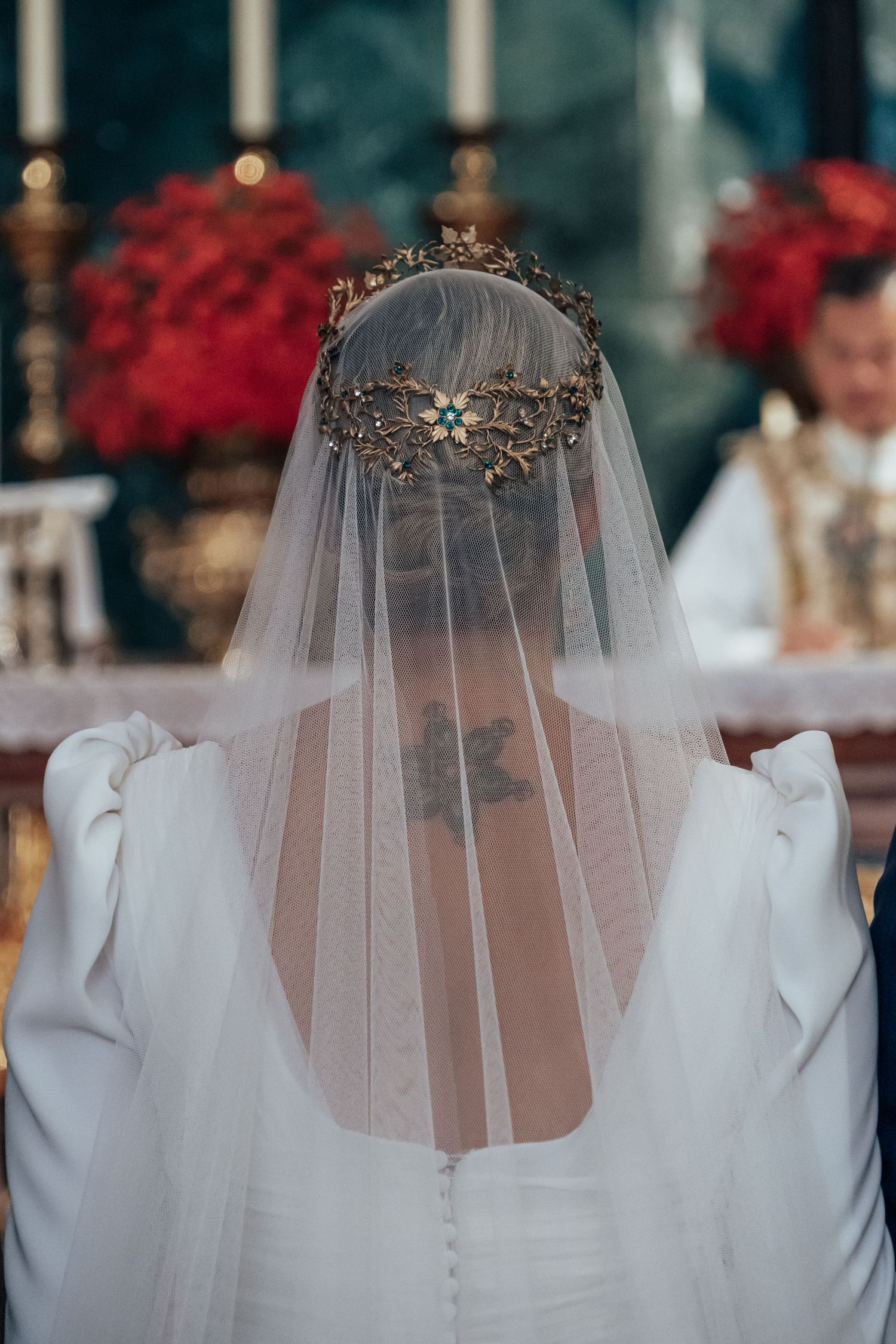 Close-up of bride wearing ornate gold crown headpiece with sheer veil draped over white wedding dress at altar.