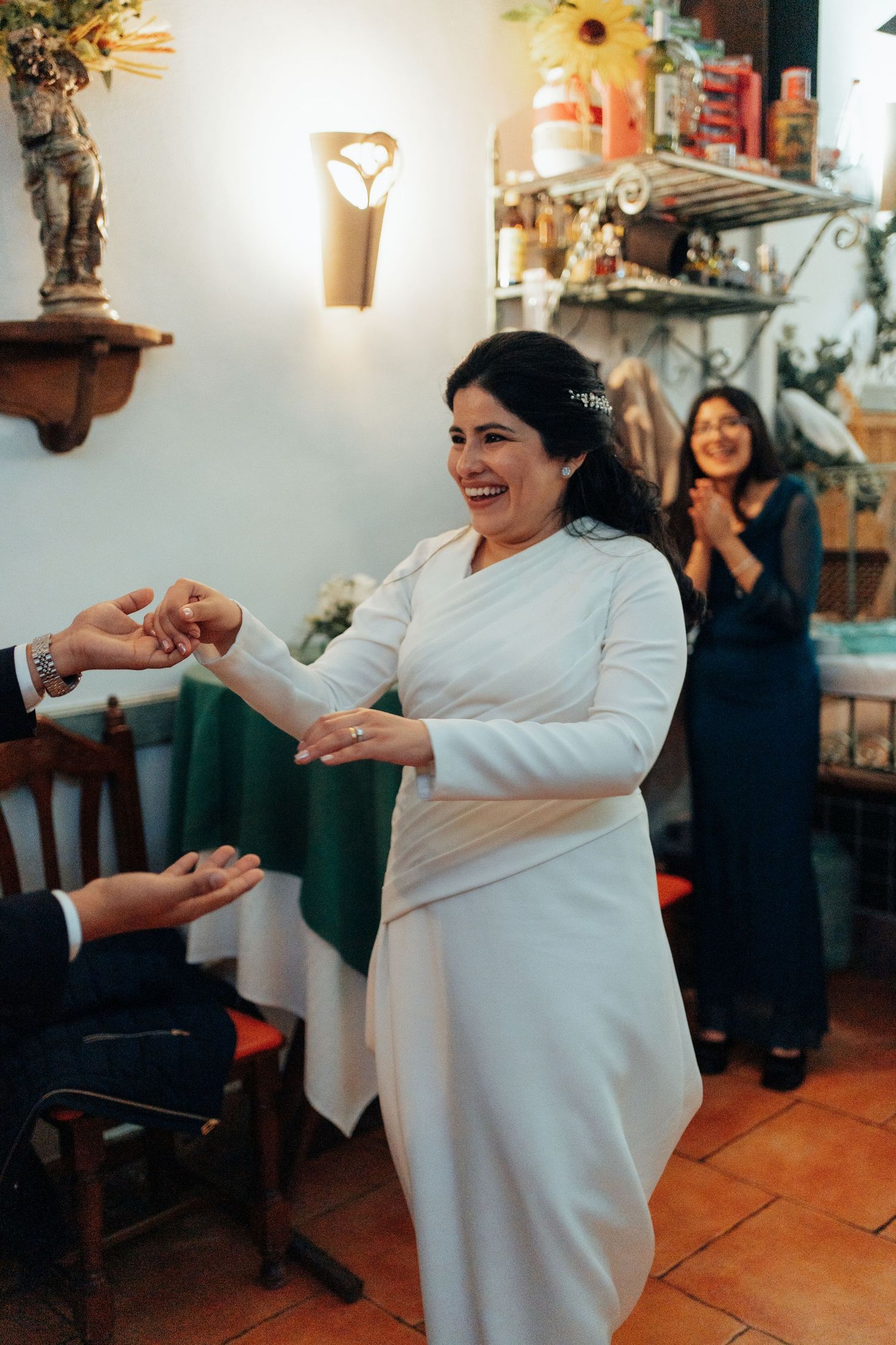 Joyful bride in white long-sleeve wedding dress laughing while holding hands during wedding reception.
