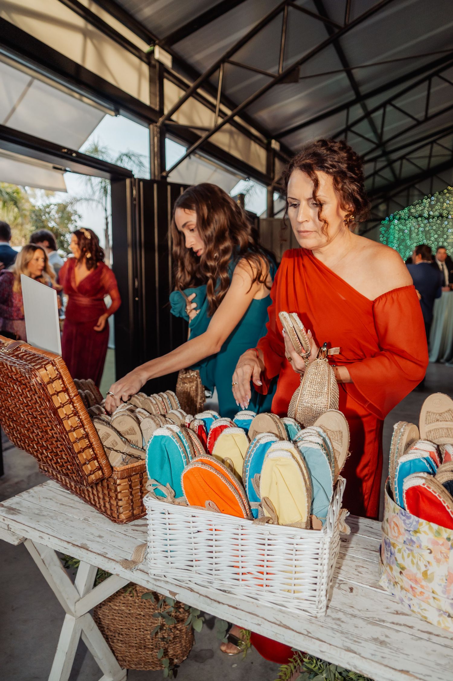 Women browsing colorful espadrilles displayed in a white wicker basket at an outdoor wedding.