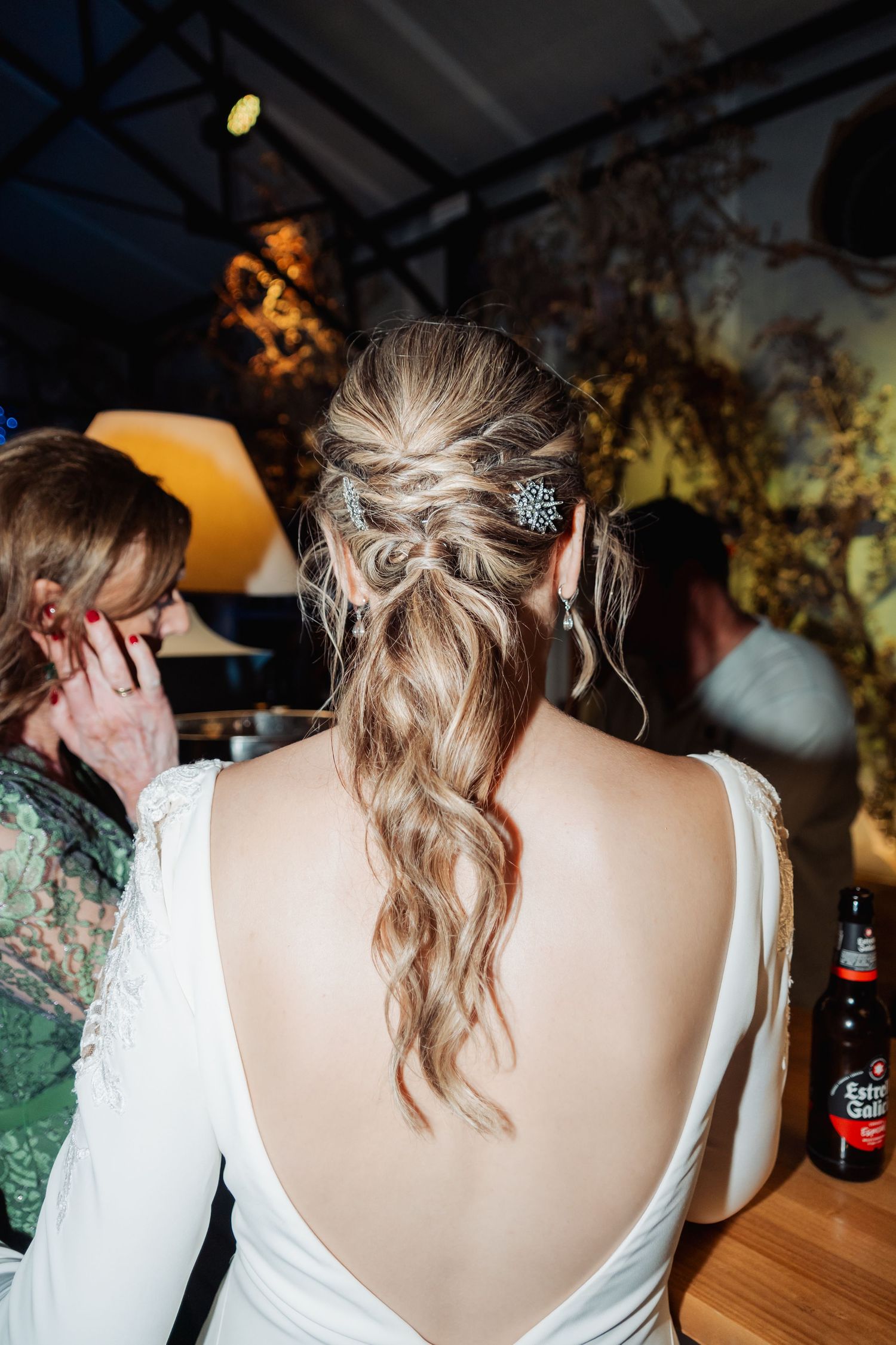 Bride with elegant braided half-updo hairstyle adorned with crystal pin in backless white wedding dress.