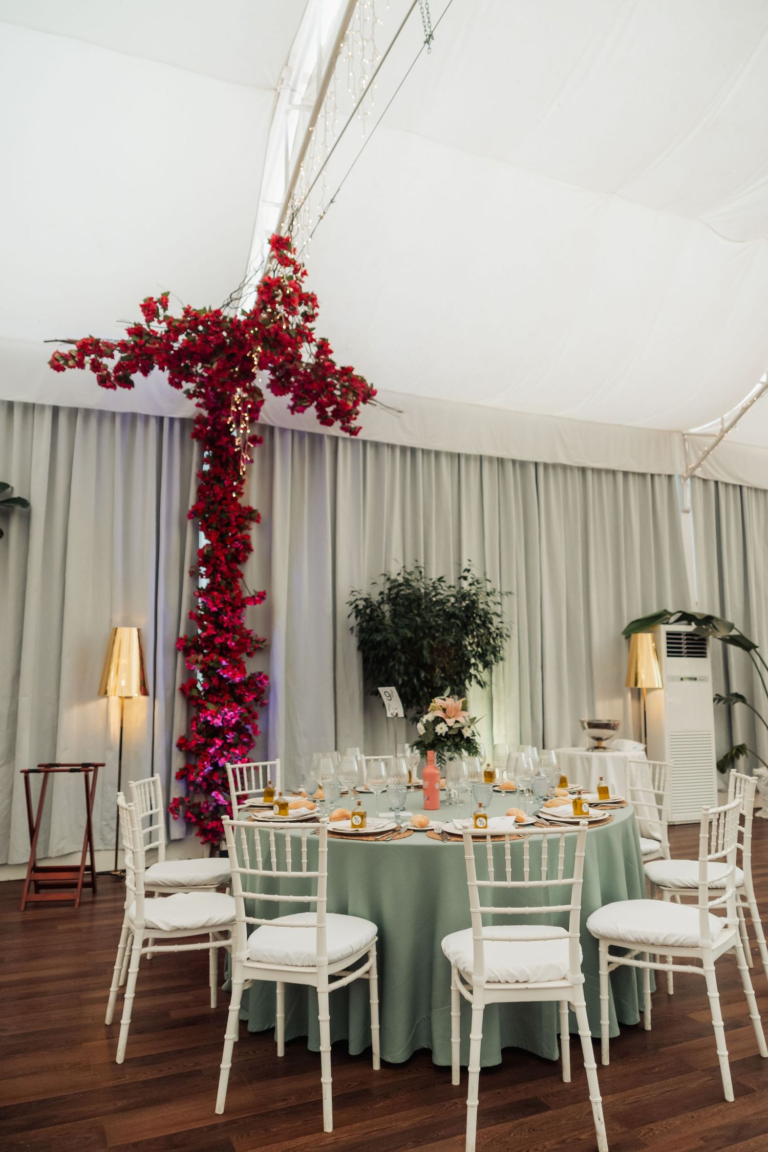 Wedding reception table with sage linen, white Chiavari chairs, and dramatic red bougainvillea installation.