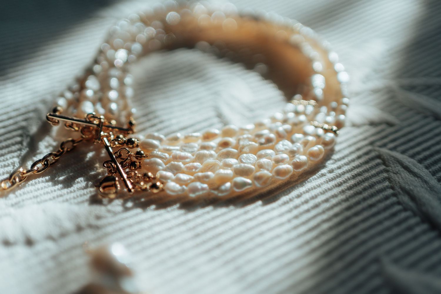 Close-up of an elegant pearl and gold bracelet with decorative clasp on soft fabric.