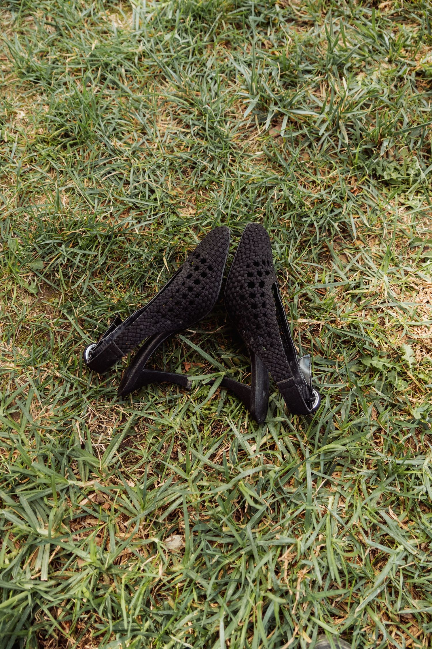 Pair of black mesh high heel shoes lying on green grass.