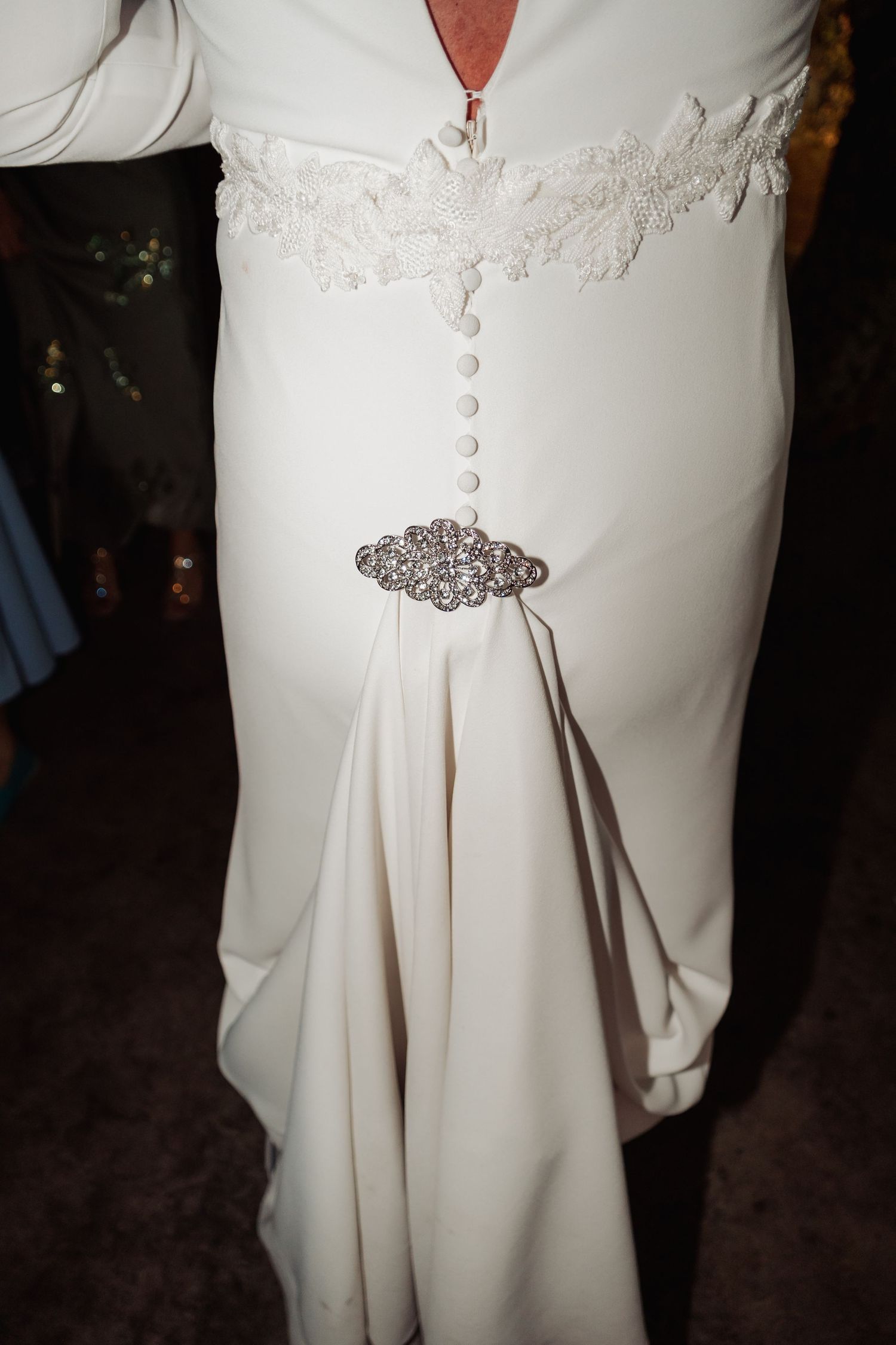 Close-up detail of a white wedding dress with lace bodice and decorative rhinestone belt brooch.