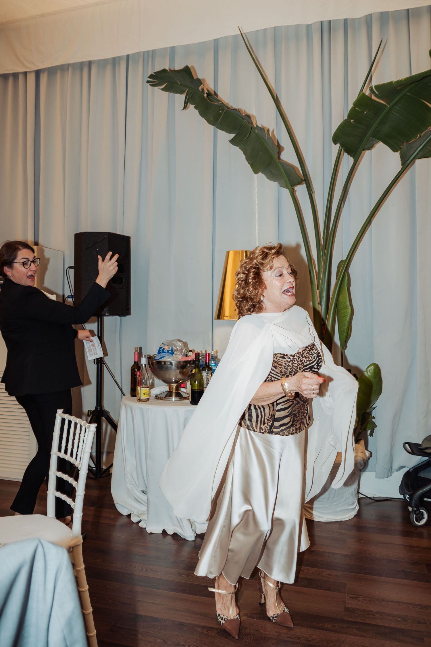Woman in white cape and animal print top dancing at an elegant wedding reception with blue curtain backdrop.