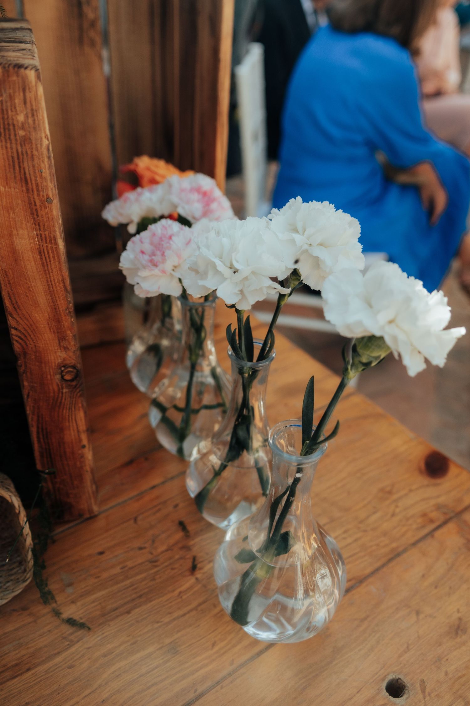 White and pink carnations in glass vases on a wooden table inside a rustic venue.