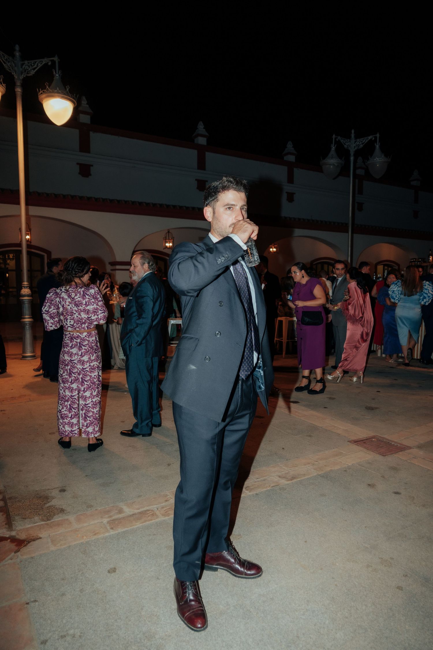 Man in gray suit standing outdoors at night during a festive evening celebration.