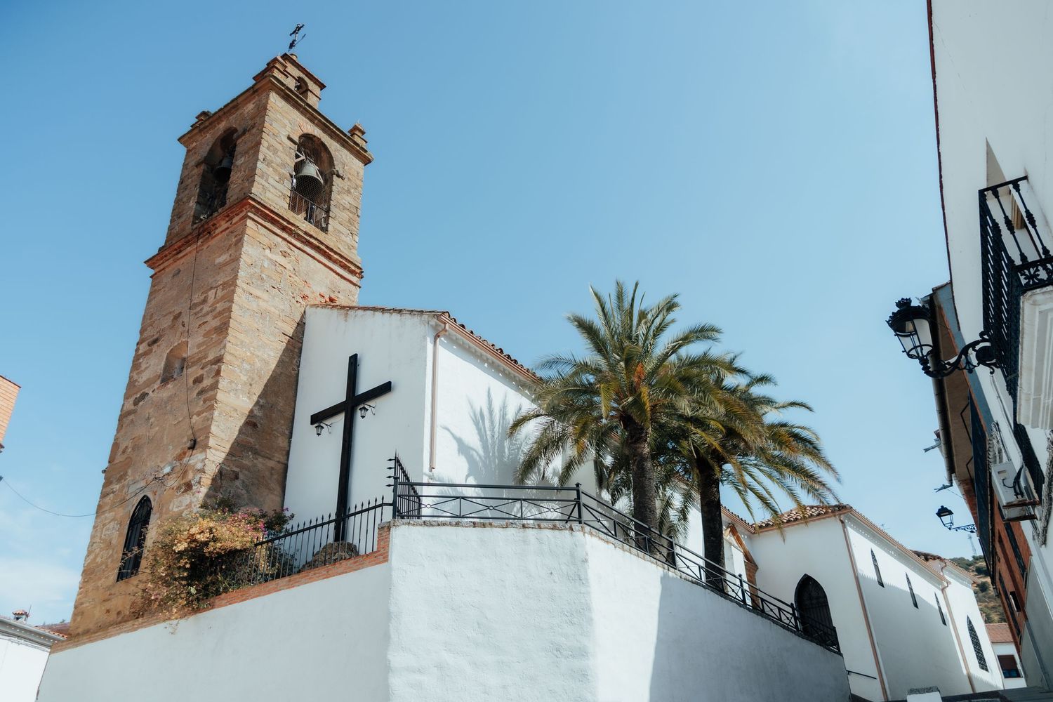 Historic Spanish church with brick bell tower, cross, and palm tree against clear blue sky.