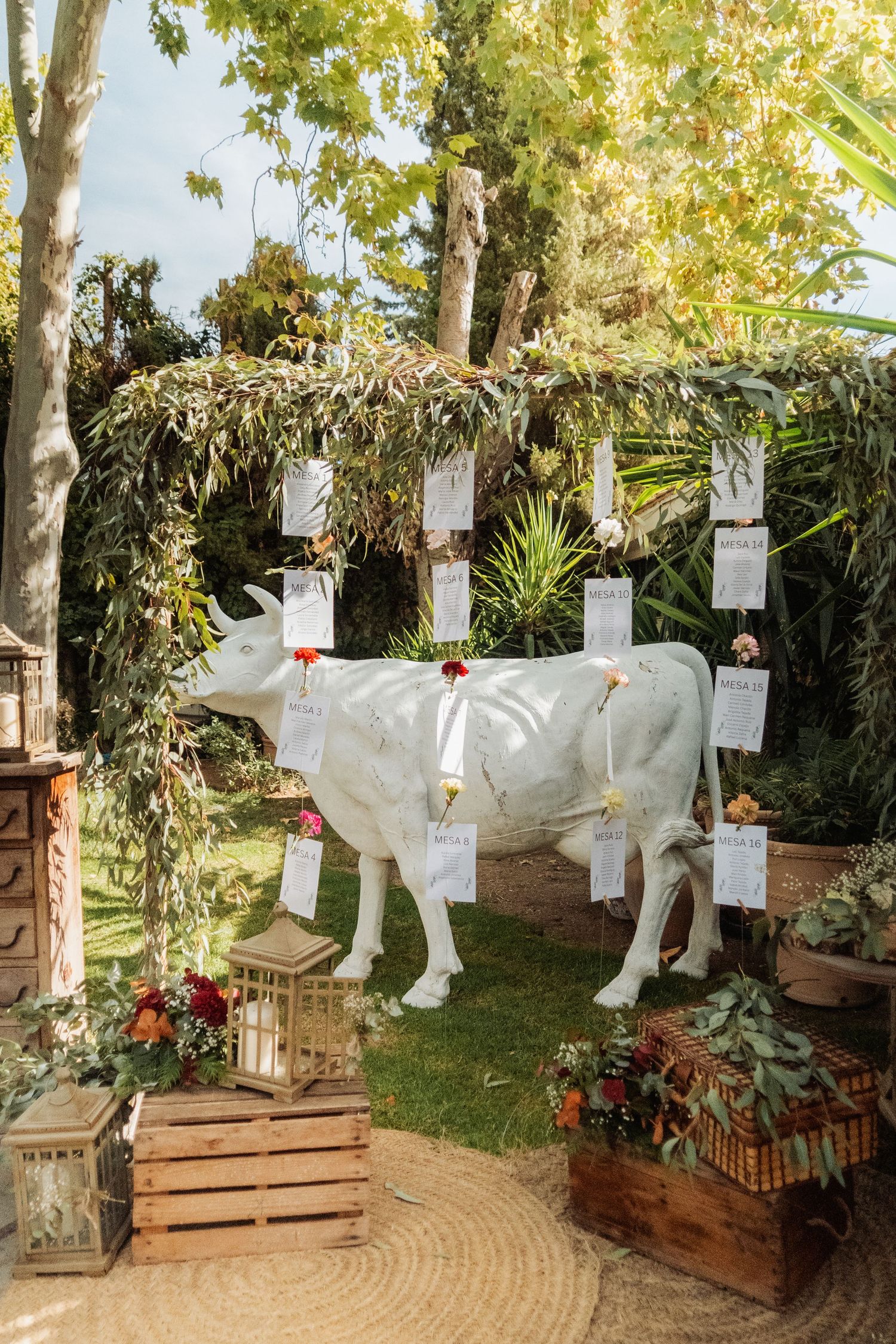 White cow statue decorated with hanging seating cards at an outdoor wedding reception.