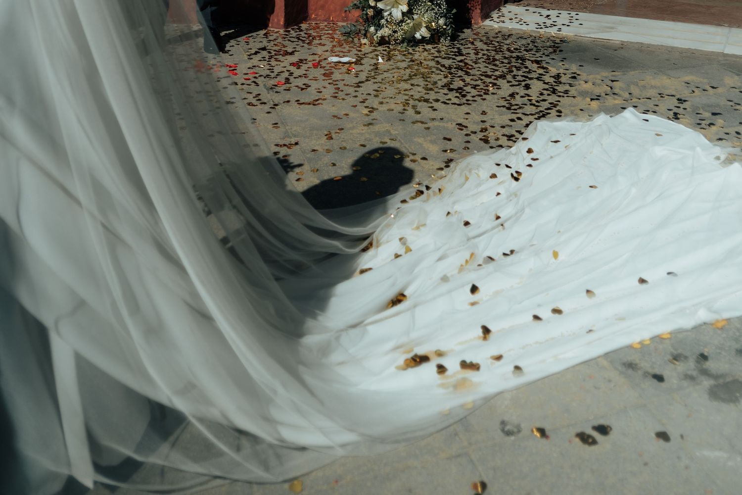 Close-up of a bride's white wedding dress train with golden confetti scattered on tiled church steps.