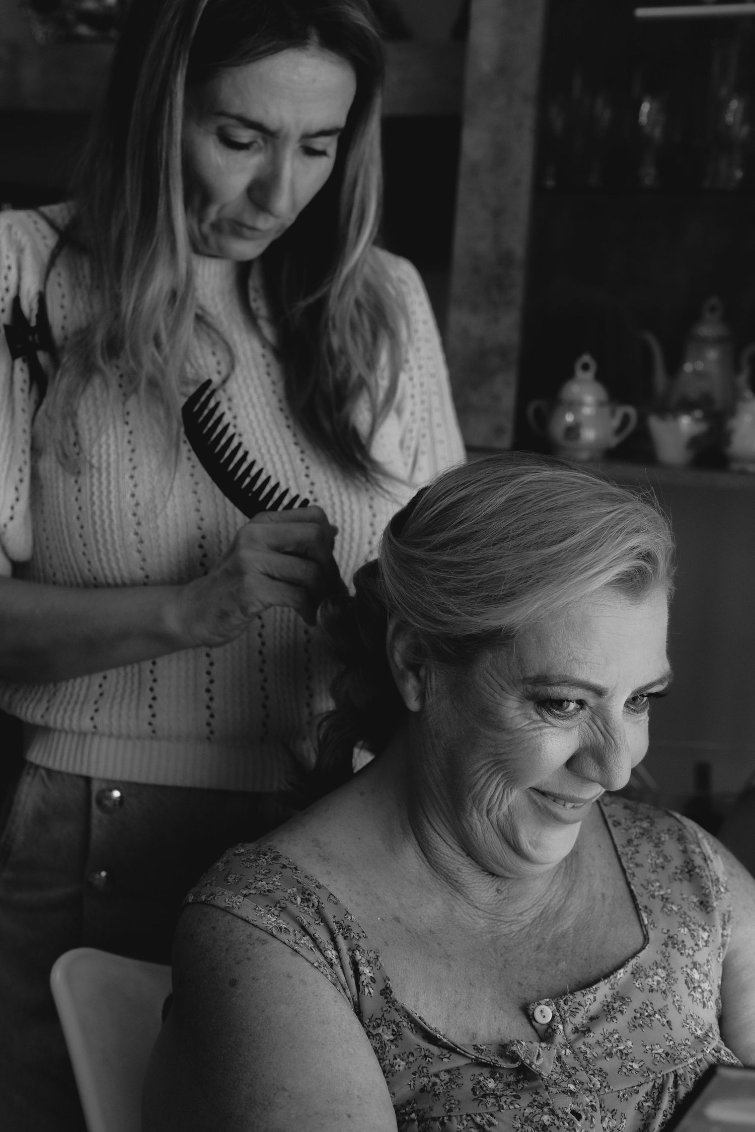 Young woman brushing older smiling womans hair in black and white photo.