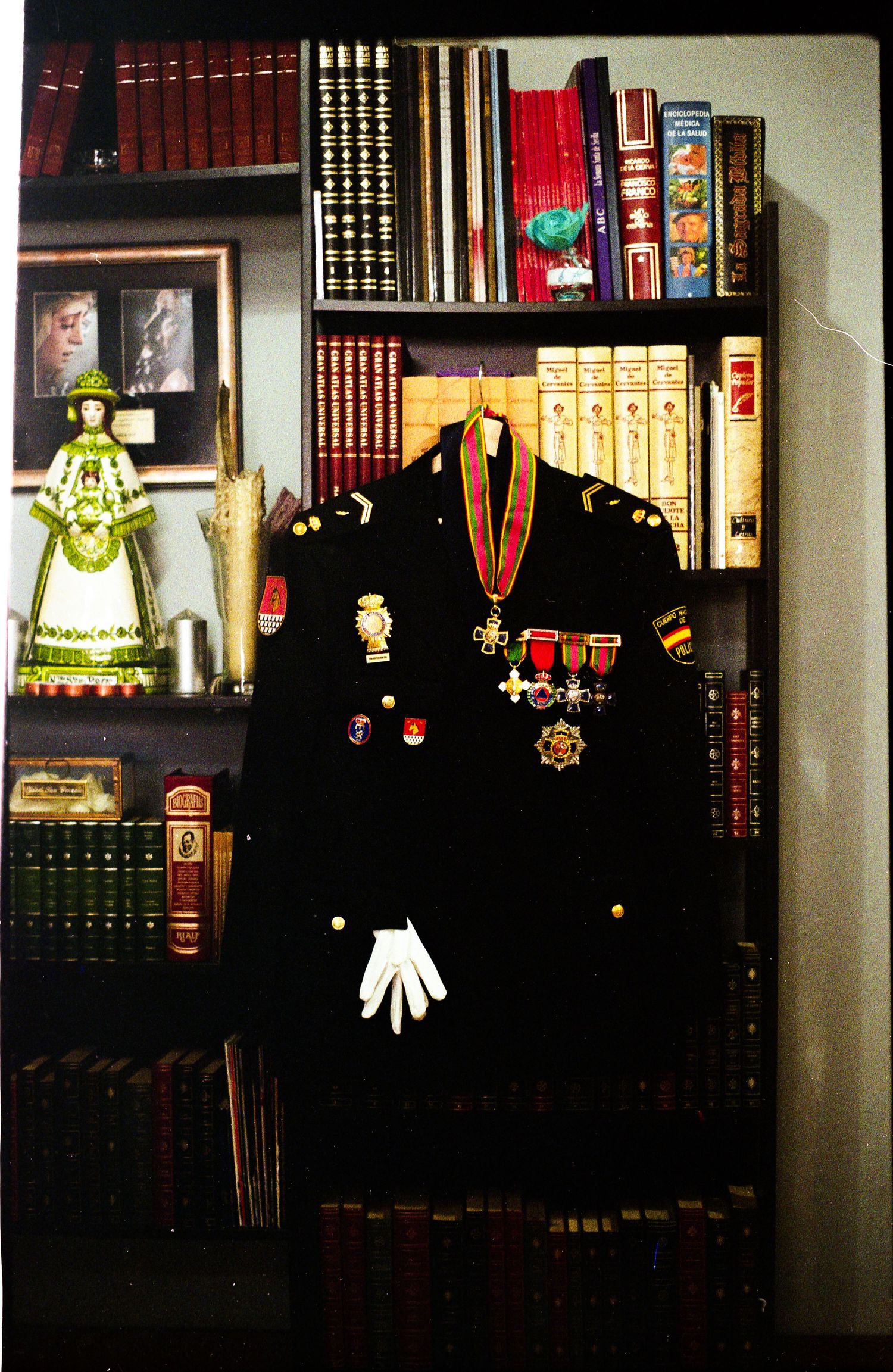 Military uniform with medals and decorations displayed on a mannequin against a bookshelf with books.