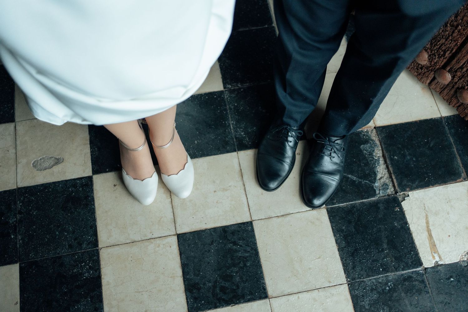 Top-down view of a bride and groom's feet on a checkered tile floor at their wedding venue.
