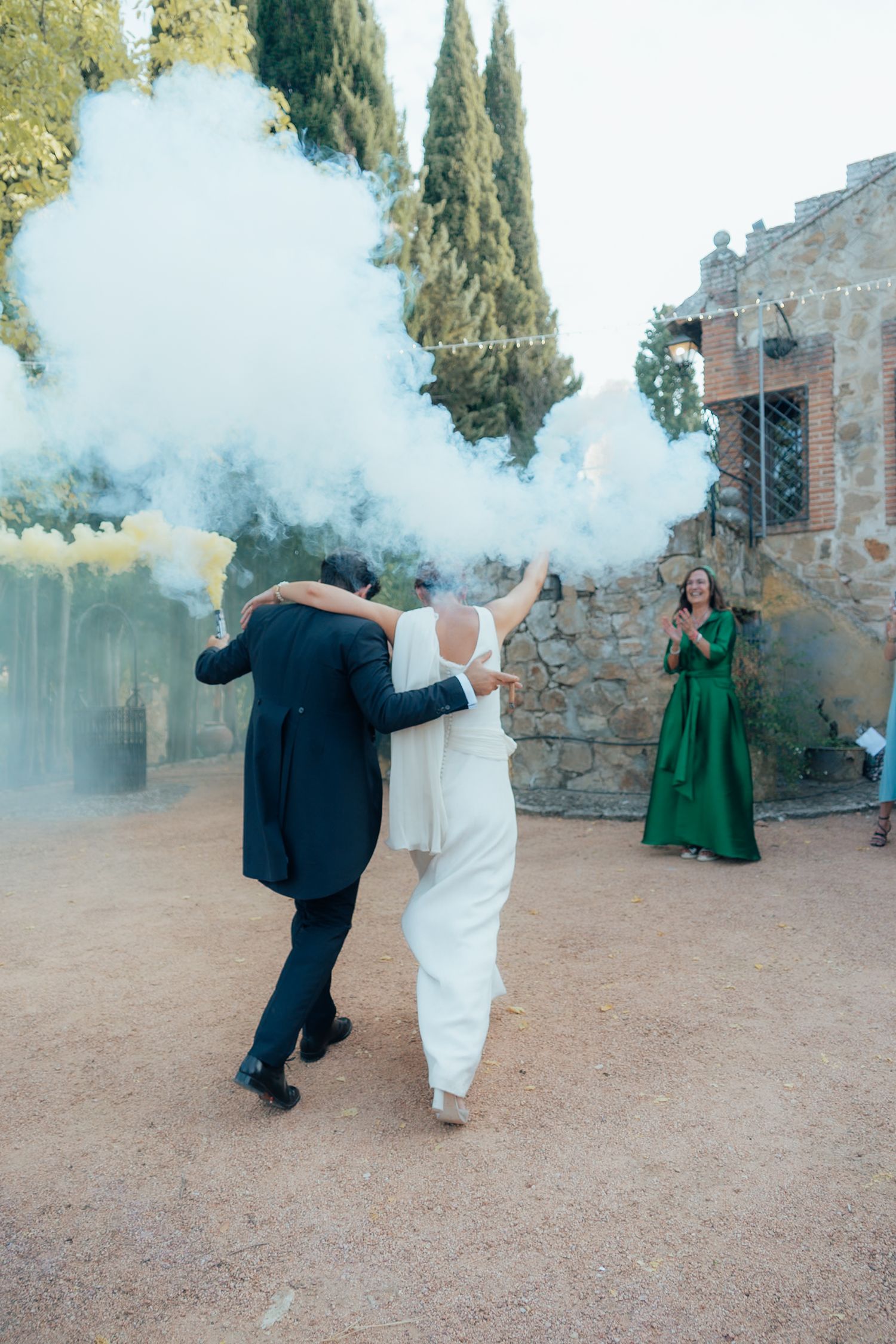 Bride and groom dancing with colorful smoke flares at rustic stone castle wedding venue.