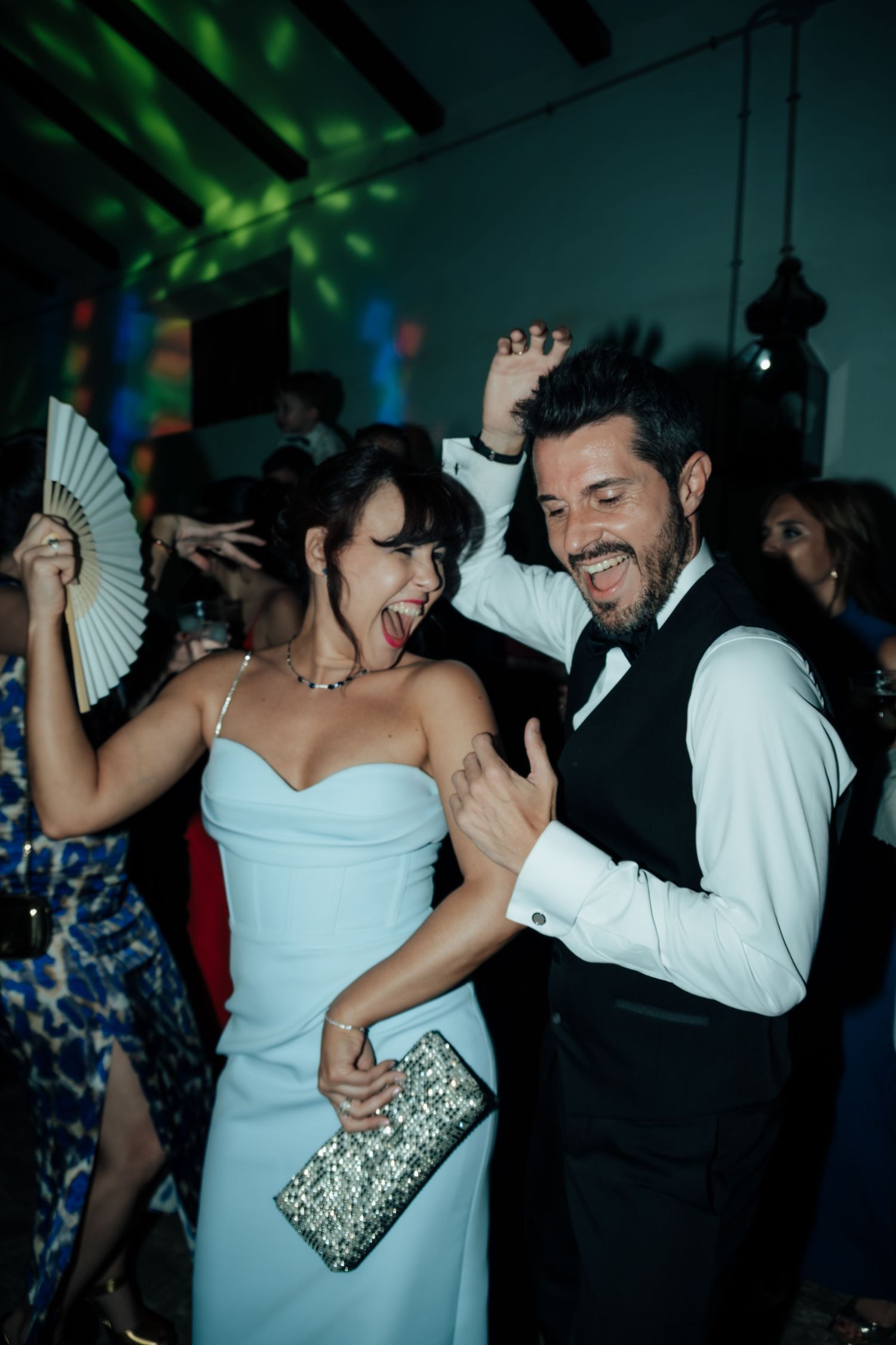 Joyful couple dancing and laughing together at lively wedding reception with disco lights.