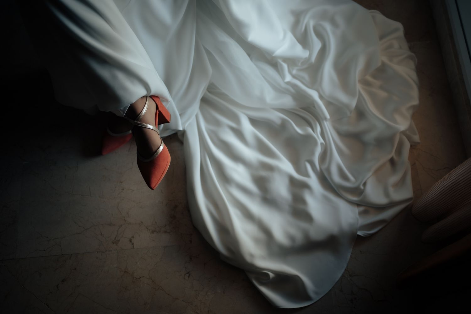 Close-up of a bride\u2019s white wedding gown train on the floor revealing red-soled designer heels beneath.