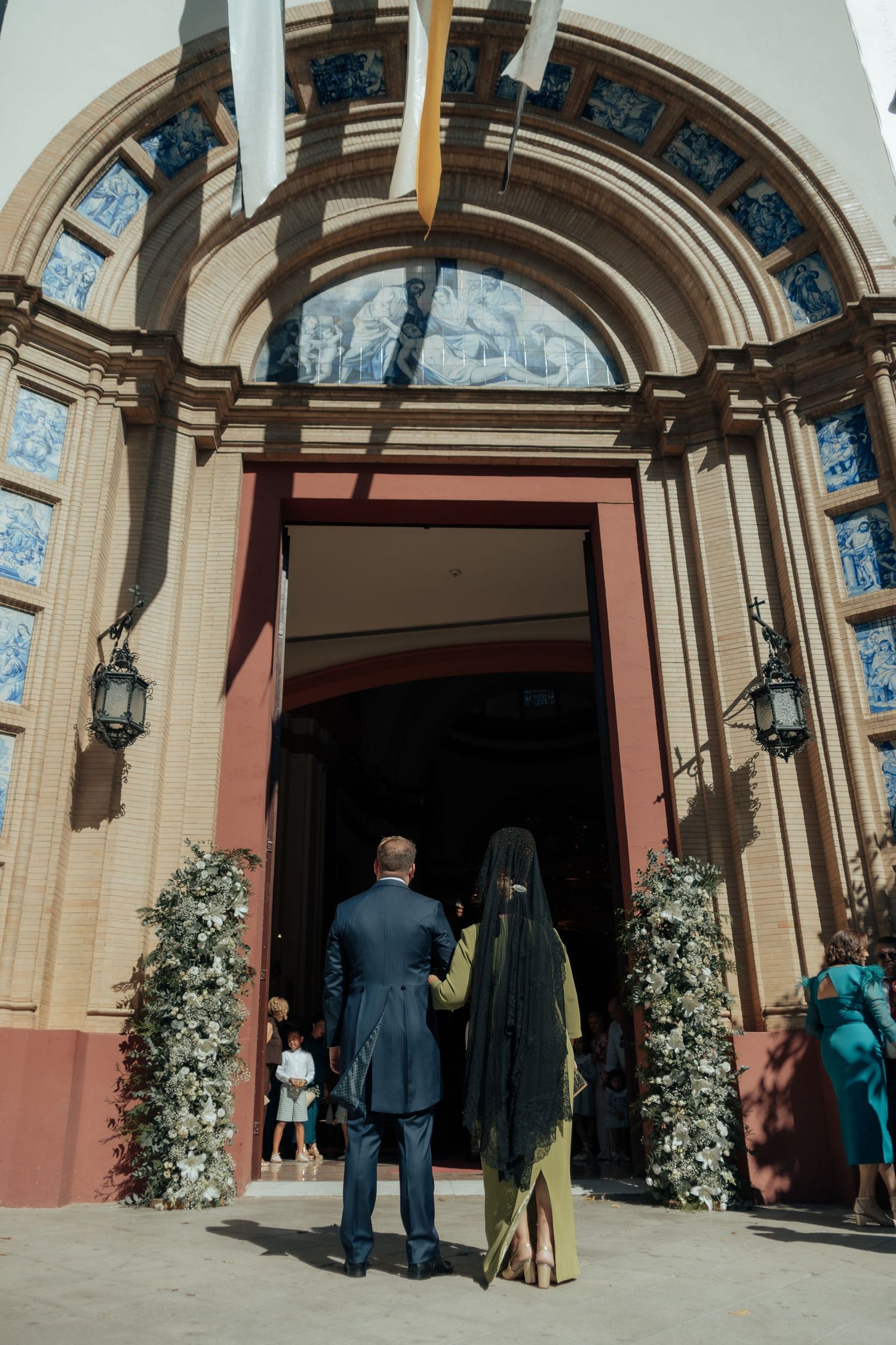 Bride and groom entering ornate church doorway decorated with floral arrangements.